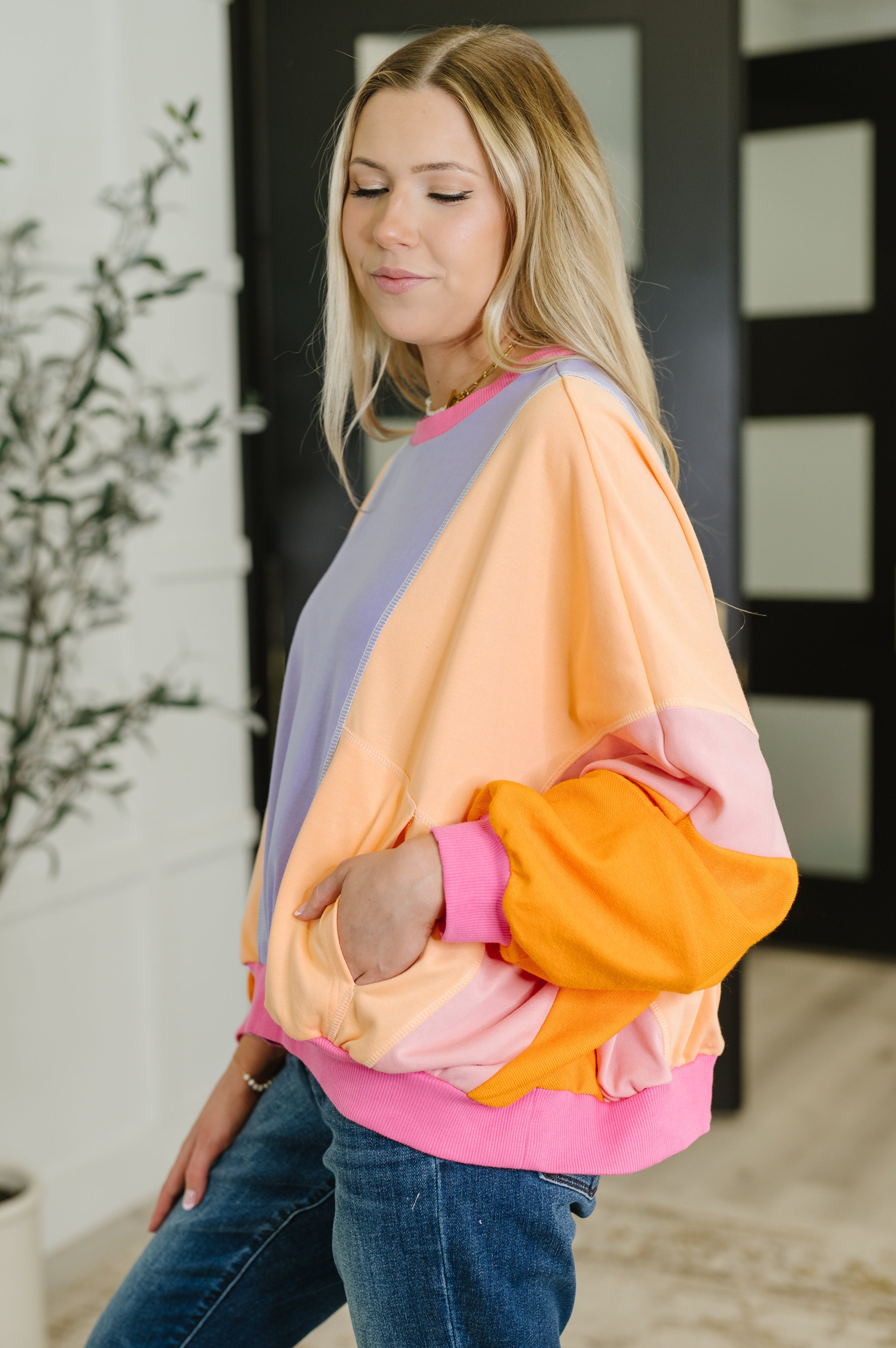 Woman modeling a muted purple and yellow color block pullover with peach dolman sleeves and pink trim indoors