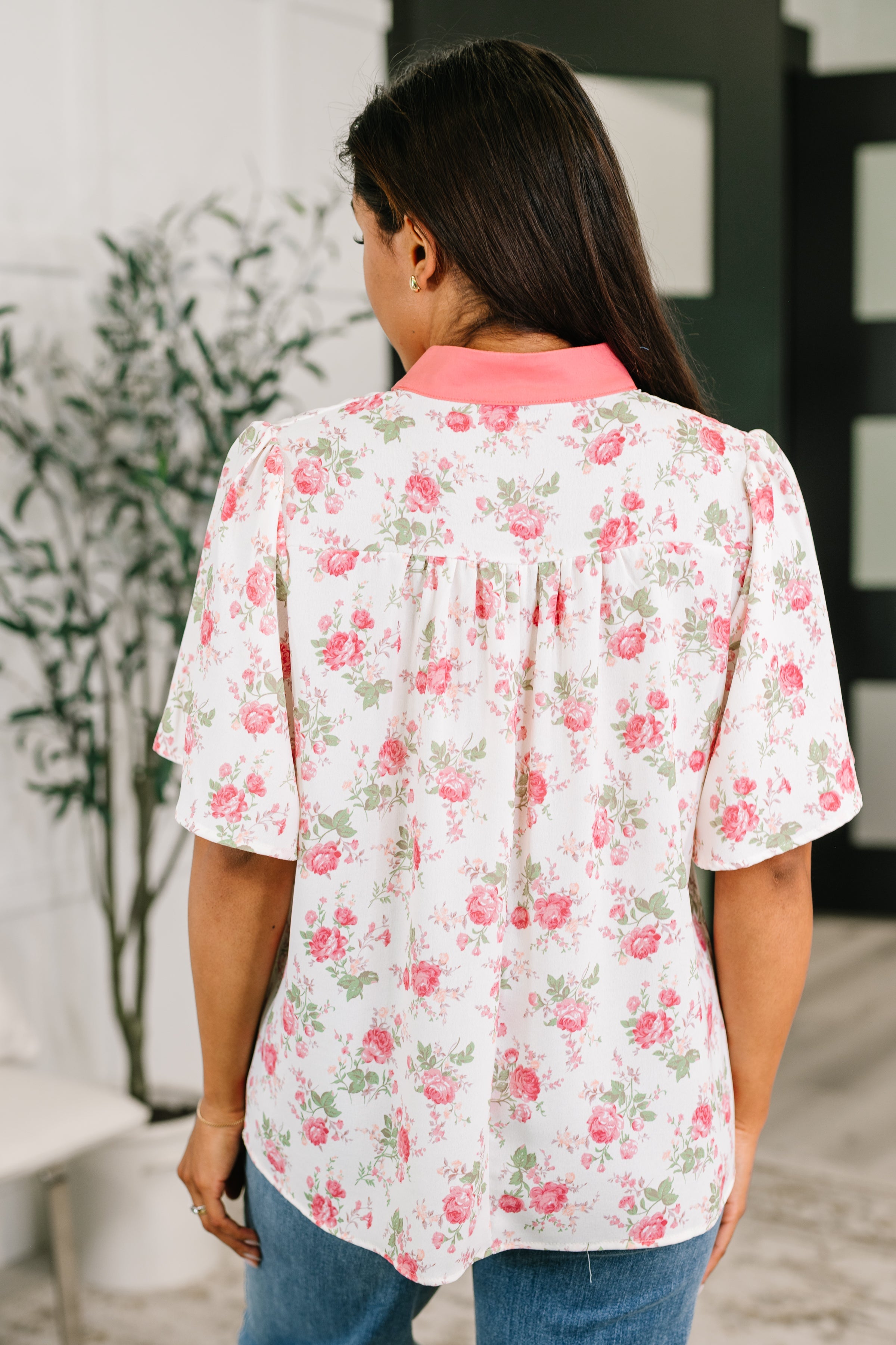 Back view of a floral blouse with coral collar and flutter sleeves in a bright, free-spirited indoor setting