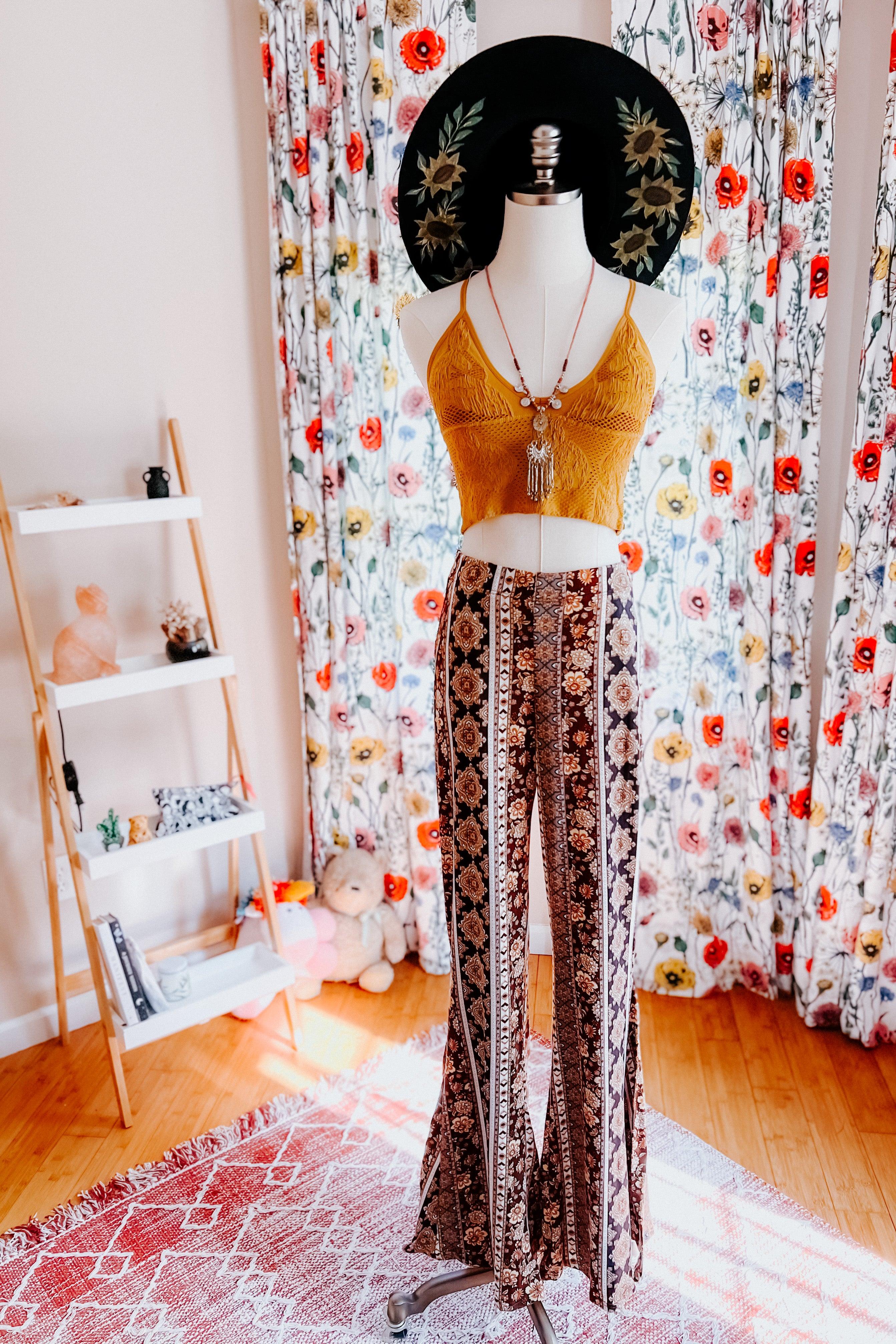 Mannequin dressed in patterned flared pants and mustard knit crop top with black floral hat in bright room