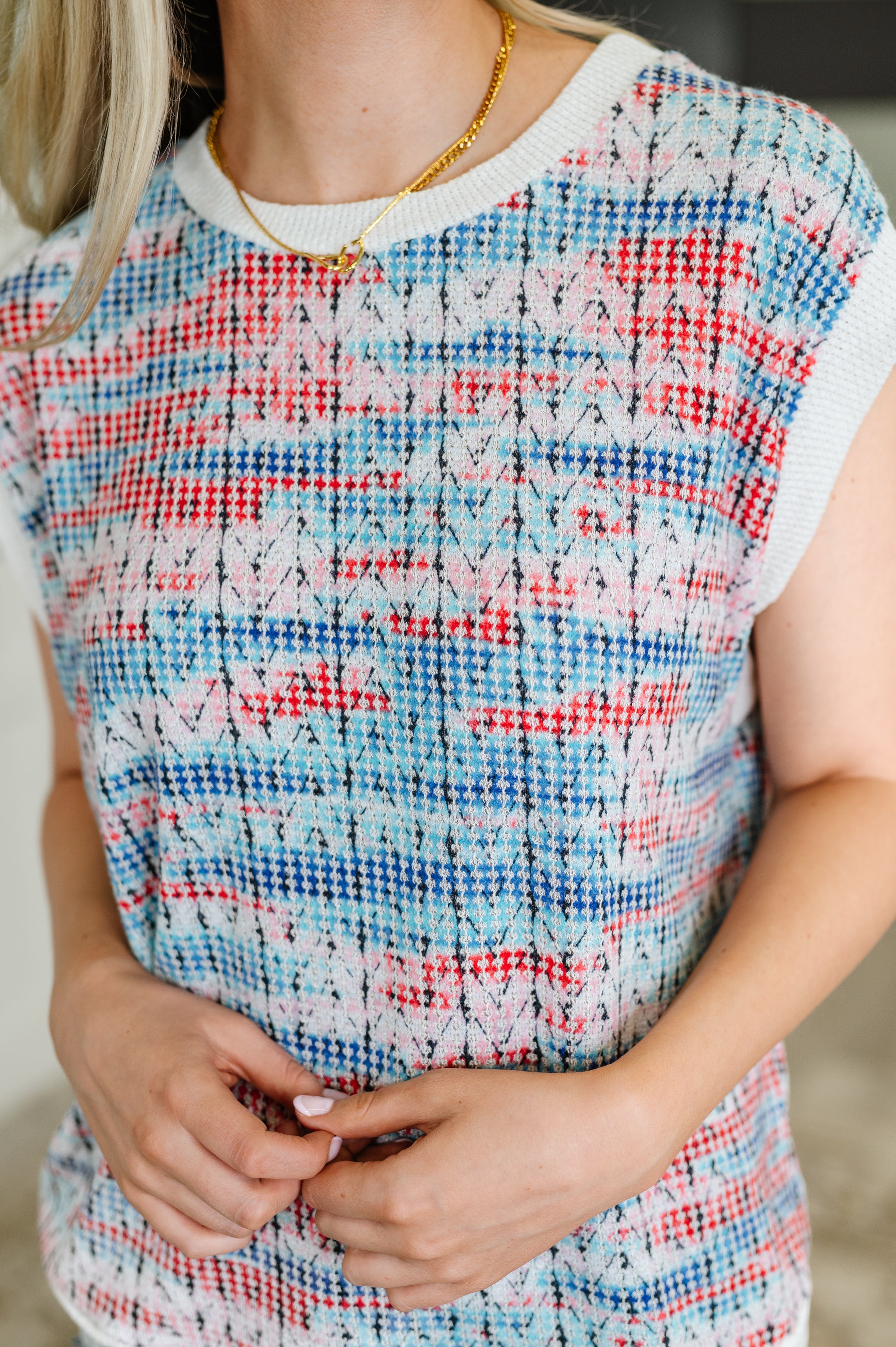 Close-up of a woman wearing a colorful blue, red, and white textured knit cap sleeve top indoors