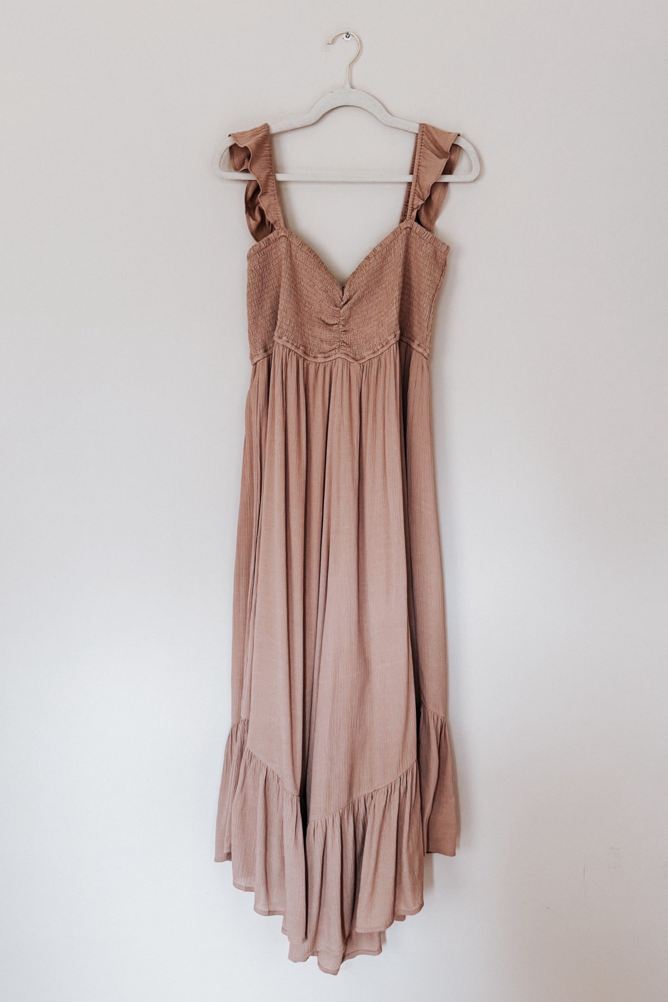 Mauve wide leg jumpsuit with smocked bodice and ruffle straps hanging on white hanger against plain wall