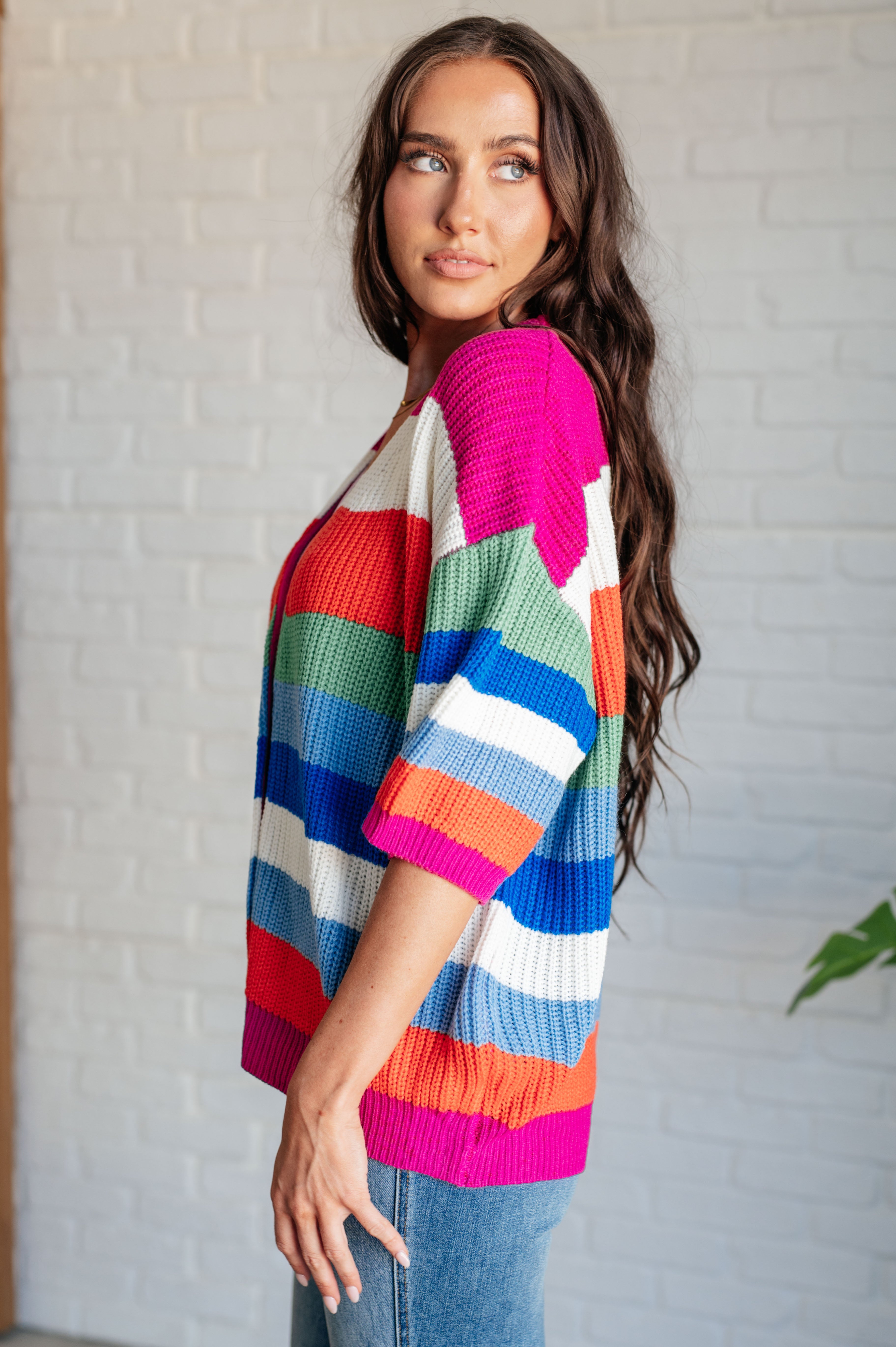 Side profile of woman wearing bold multicolor striped button-down cardigan with vibrant pink, blue, green, and orange tones