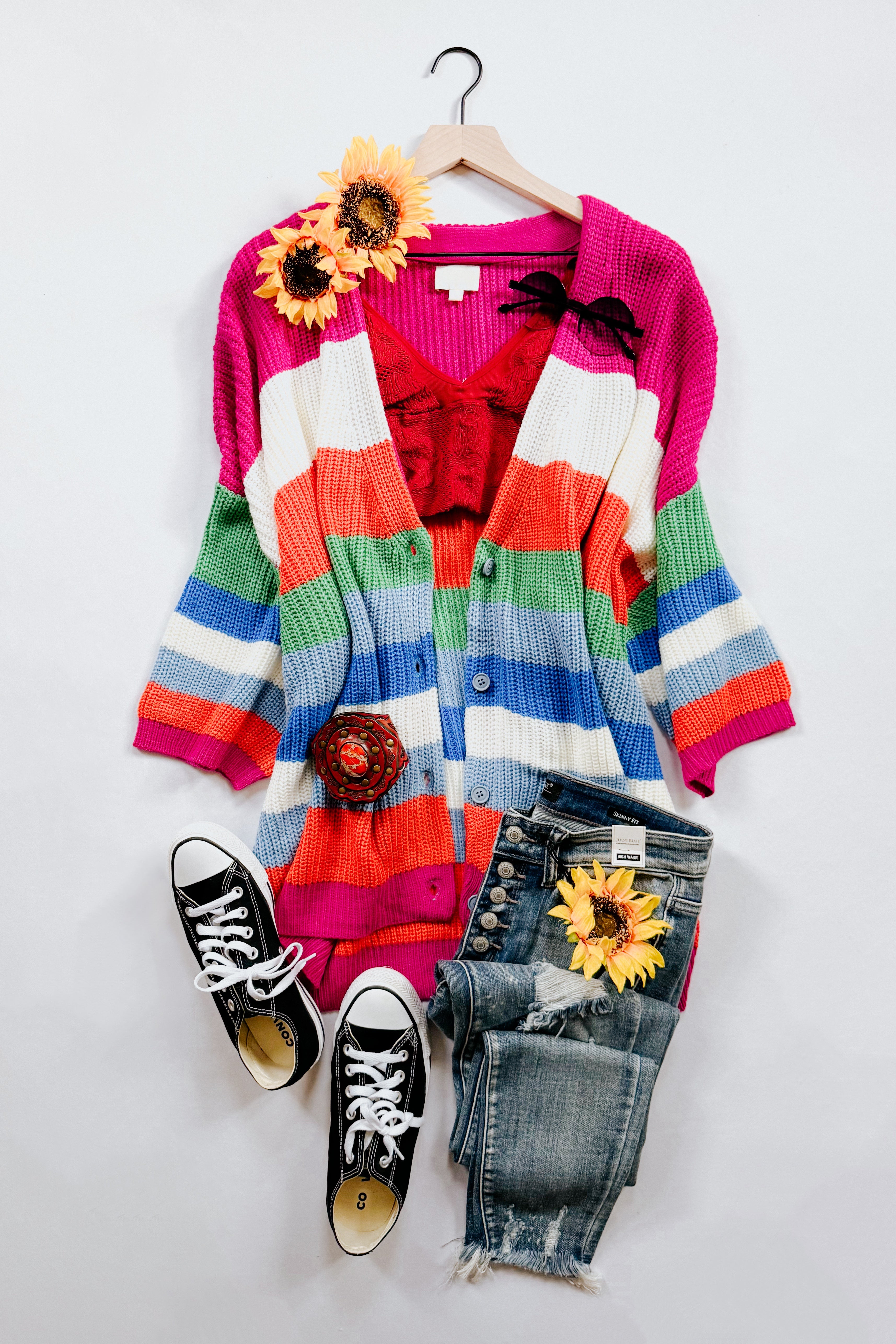 Striped chunky knit cardigan in bright colors paired with red top, distressed button-fly jeans, and black sneakers flat lay