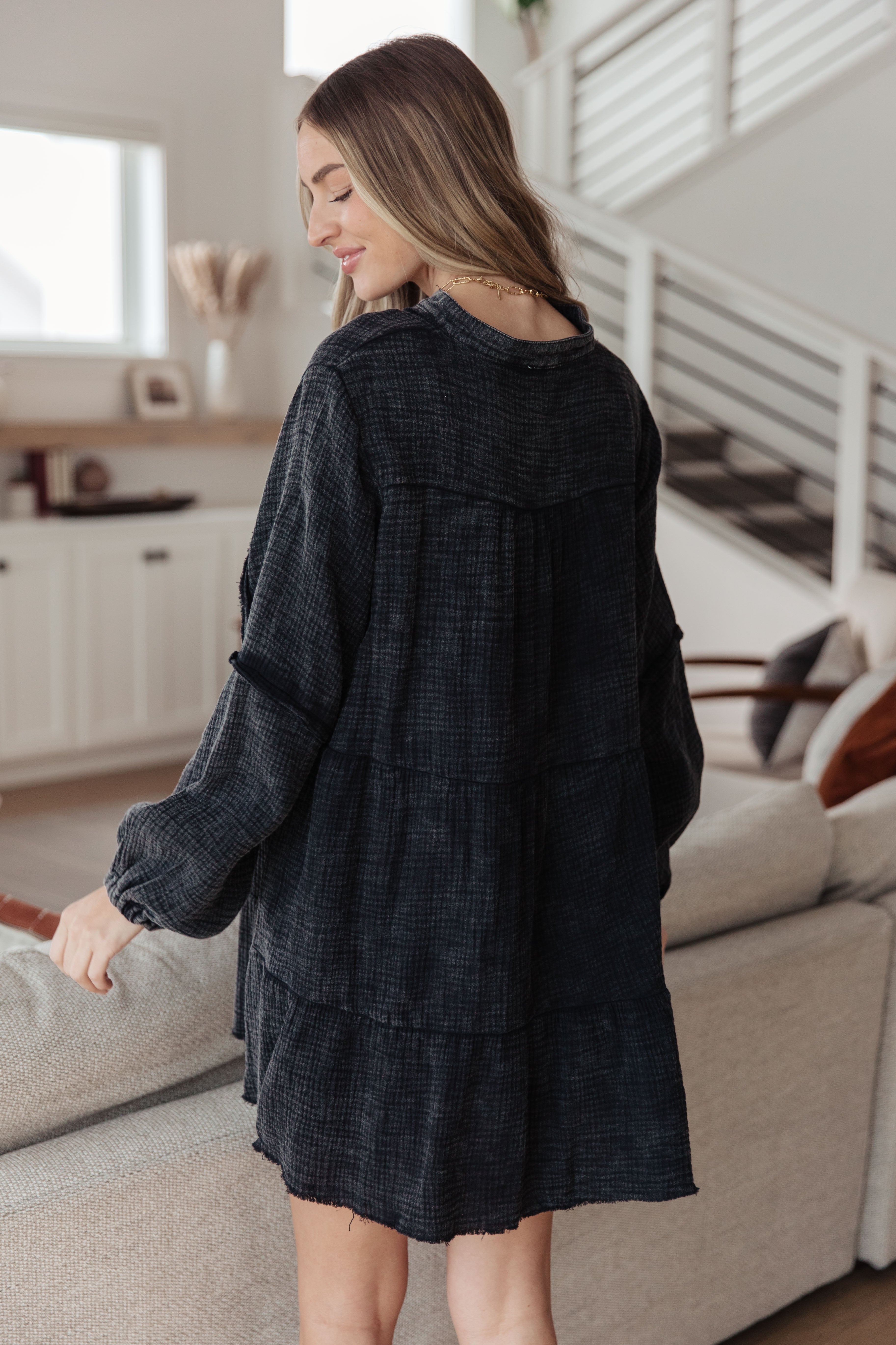 Woman wearing loose dark mineral wash tiered dress with balloon sleeves standing indoors by couch