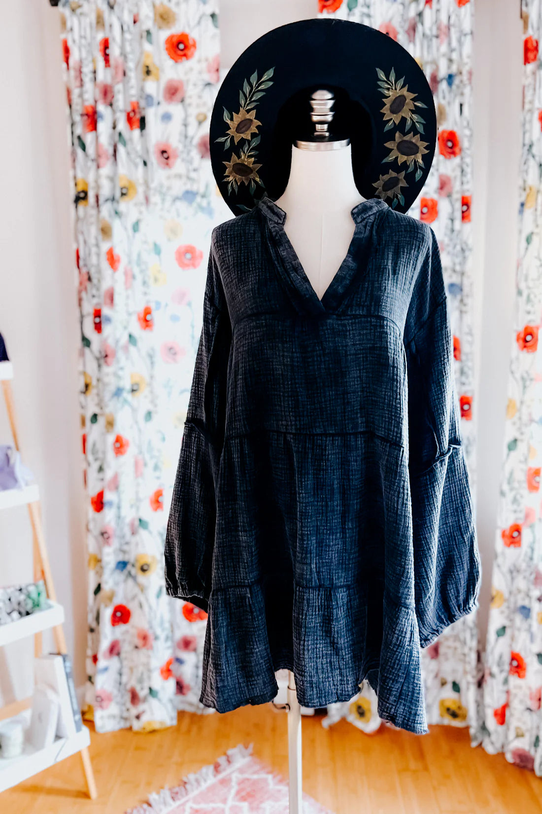 Mannequin dressed in loose dark mineral wash V-neck dress with long sleeves and tiered hem wearing black floral wide-brim hat