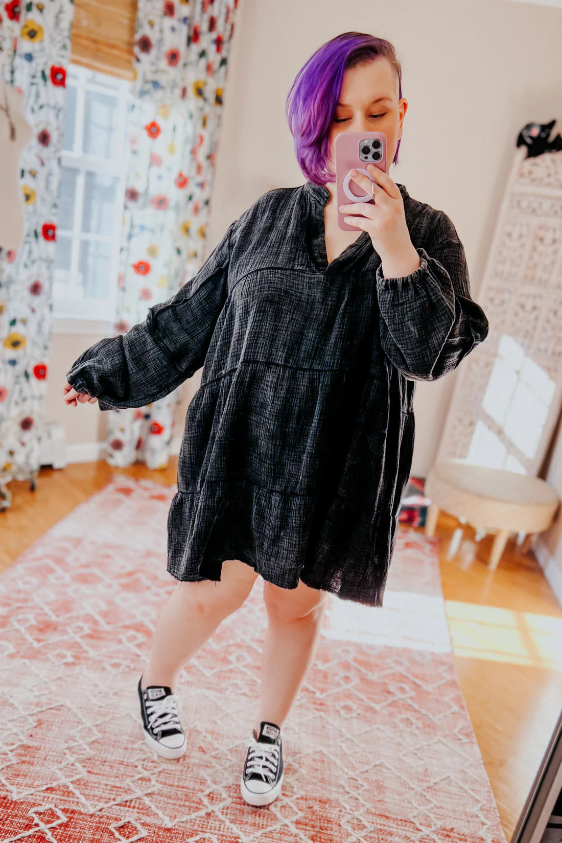 Woman with purple hair taking selfie wearing loose black mineral wash V-neck dress and black low-top sneakers indoors
