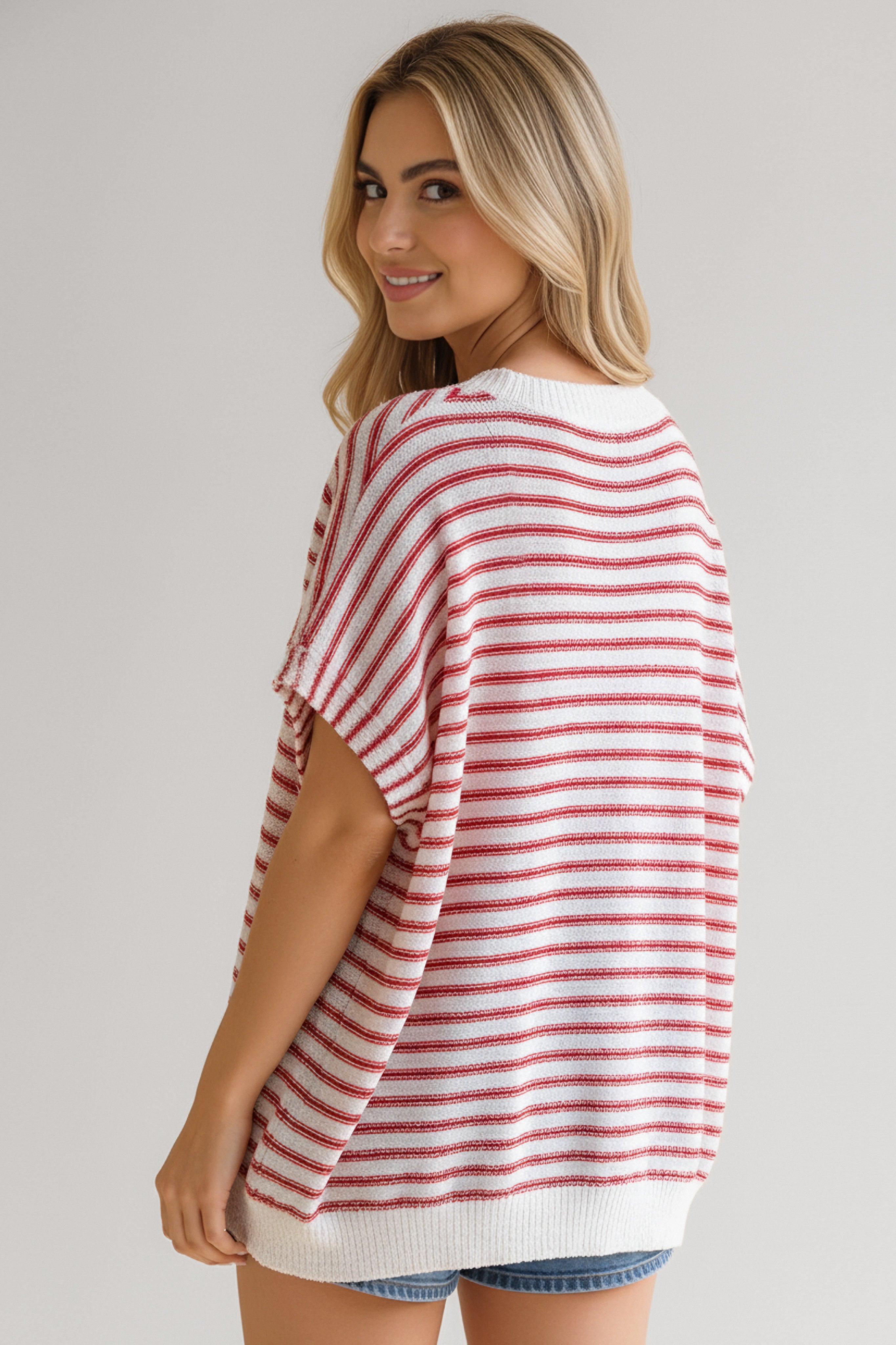 Woman wearing relaxed fit red and white striped knit top with short sleeves and denim shorts smiling over shoulder