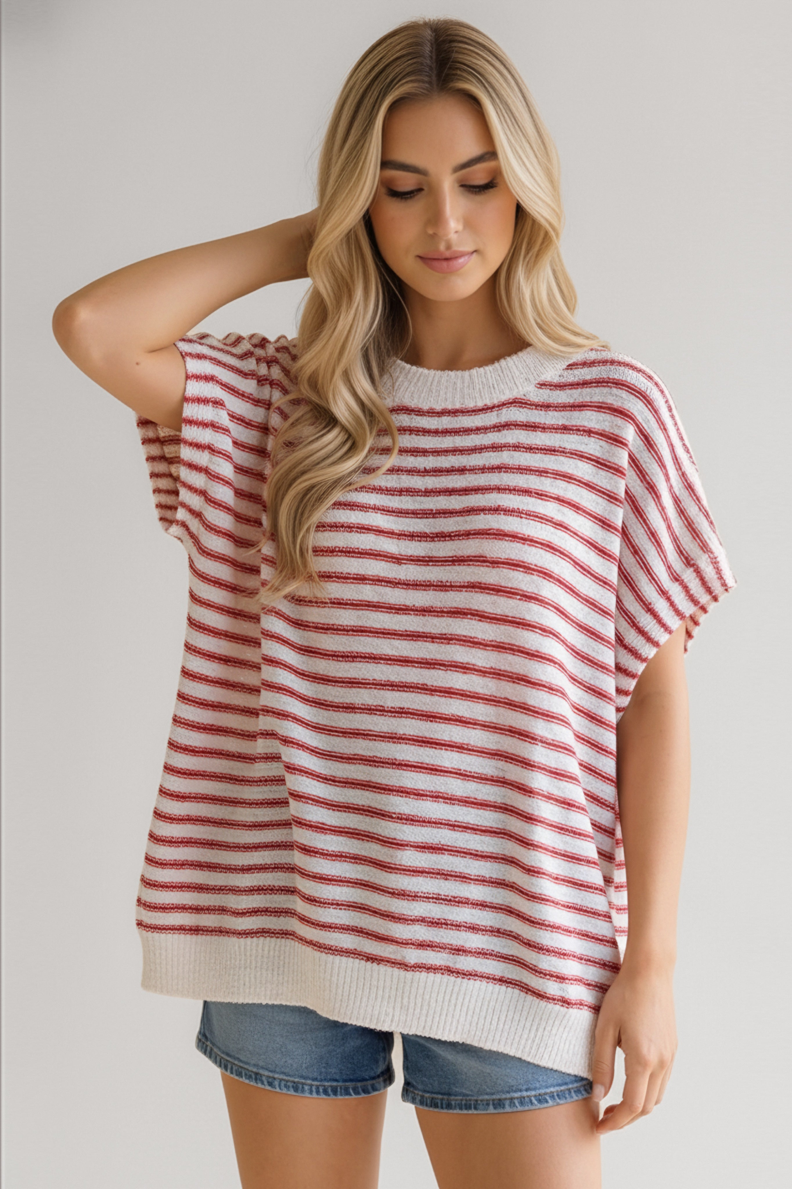 Woman wearing relaxed fit red striped knit top with short sleeves paired with denim shorts in casual pose