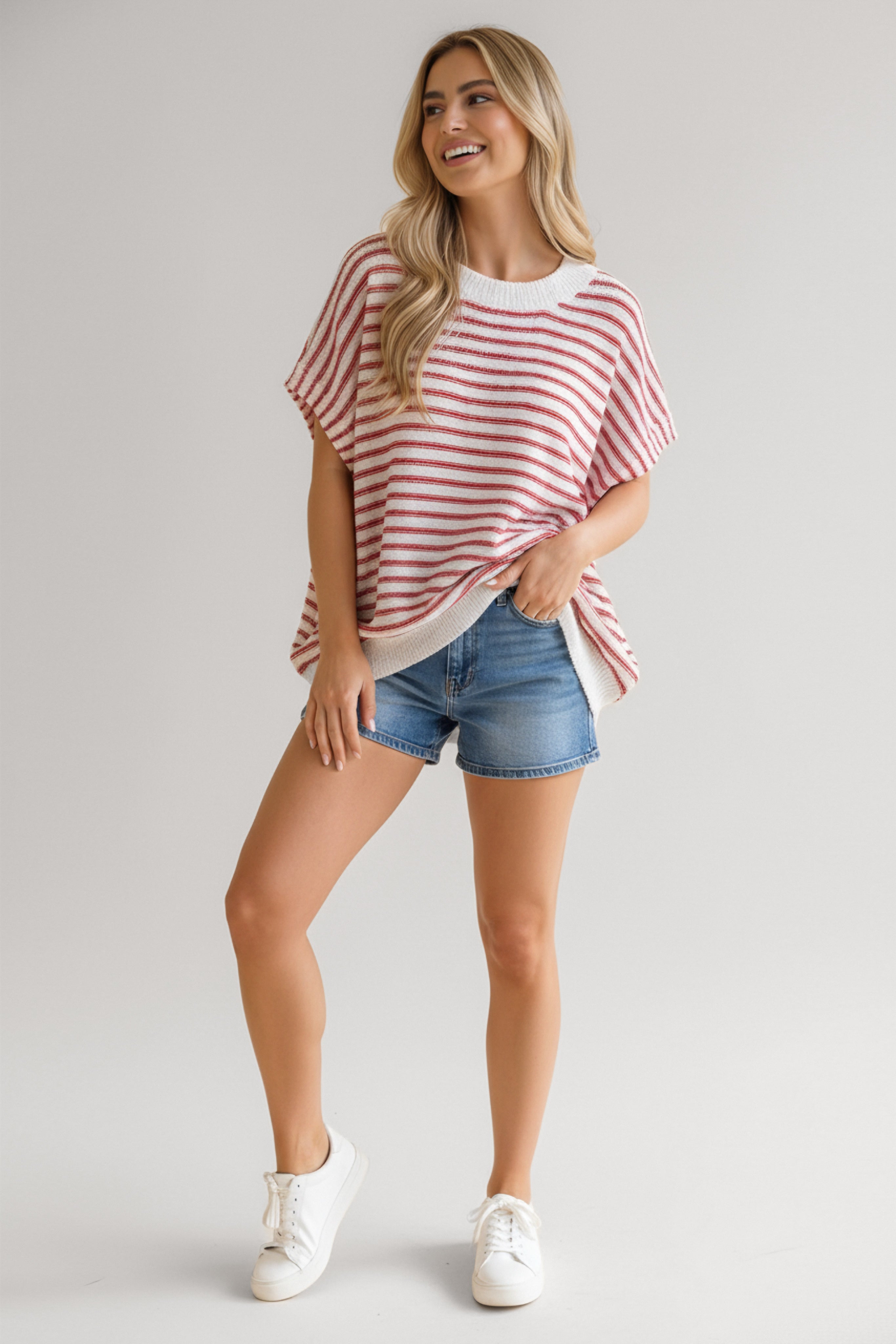 Woman wearing a relaxed fit red striped knit top paired with casual denim shorts and white sneakers smiling