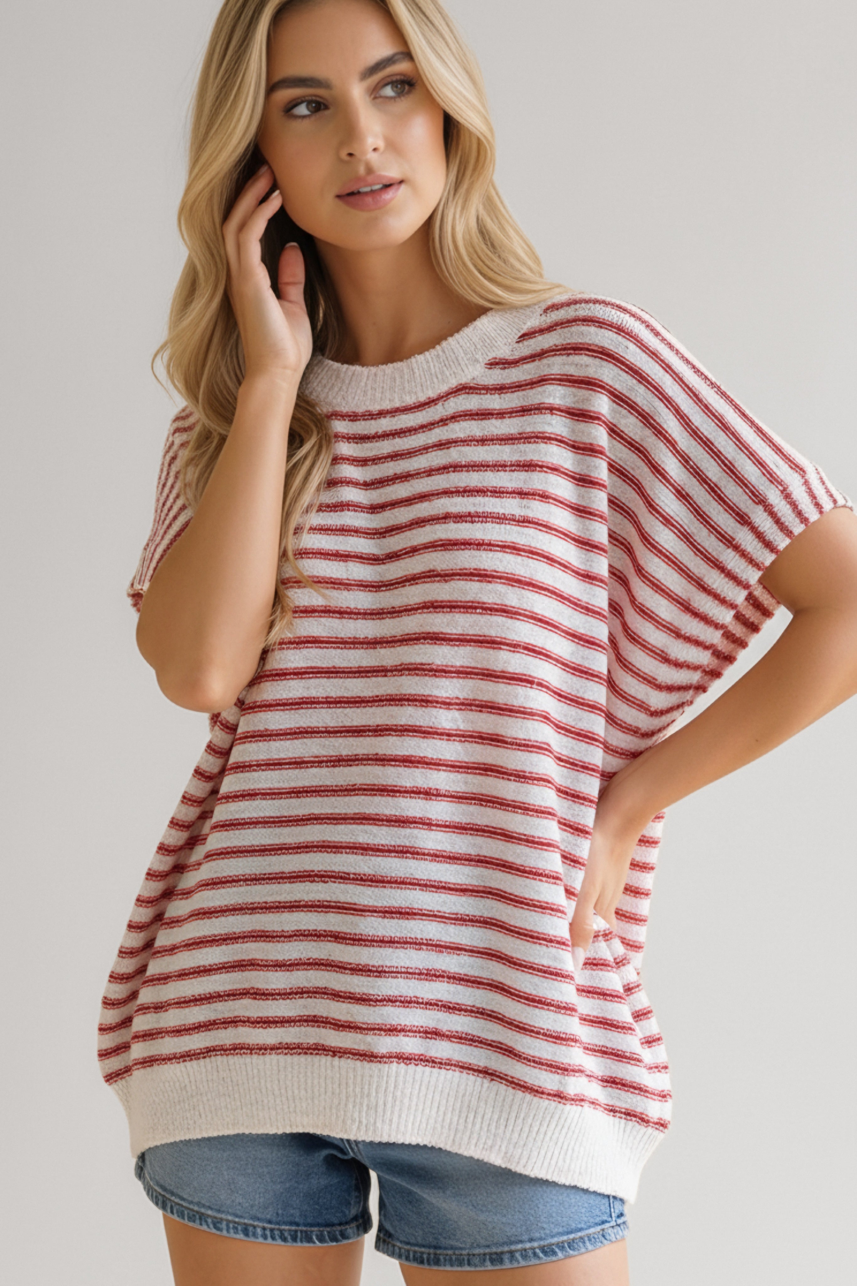Woman wearing a loose red striped knit top paired with denim shorts in relaxed, casual pose