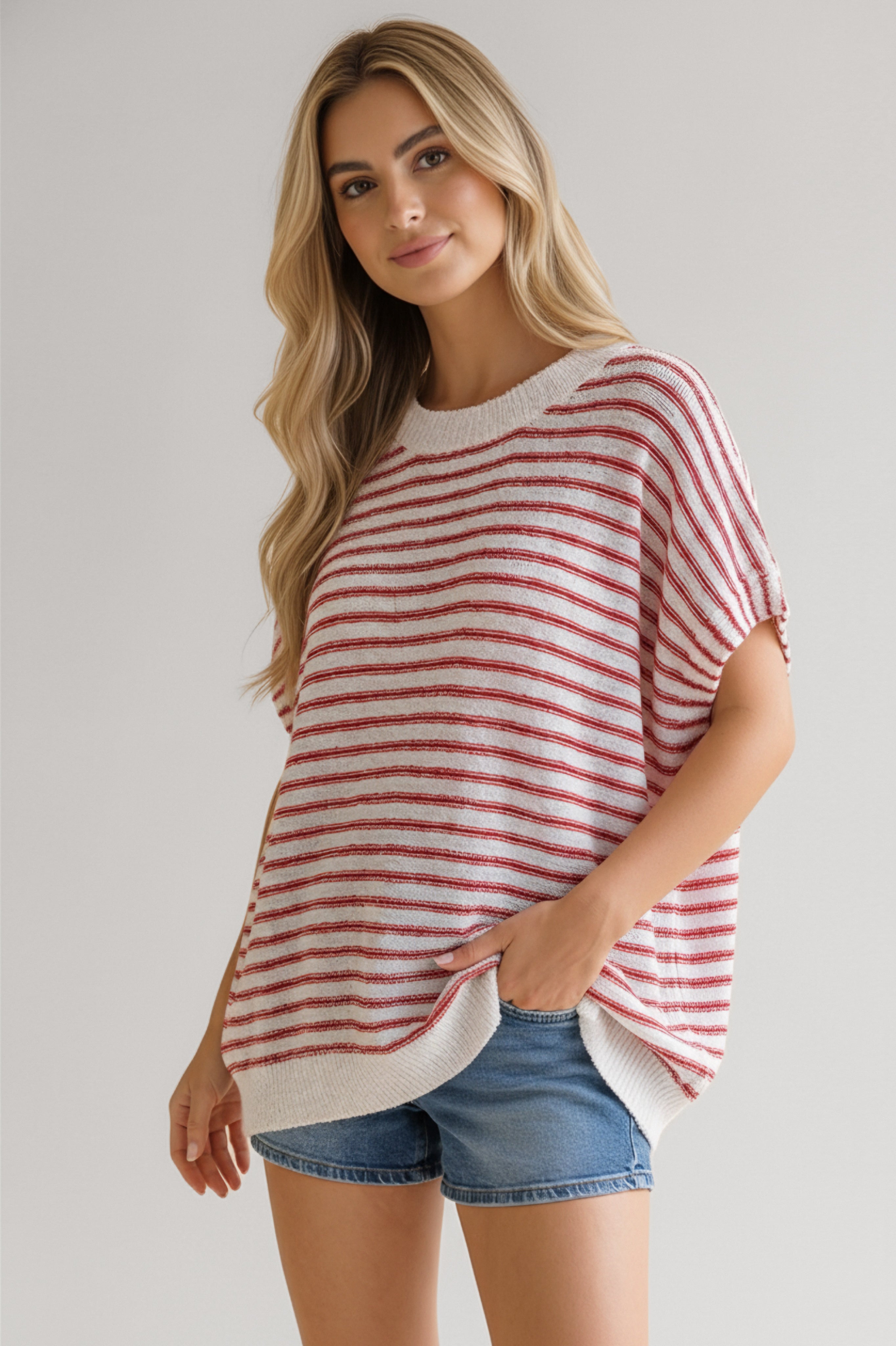 Woman wearing loose red and white striped knit top paired with casual blue denim shorts in relaxed pose