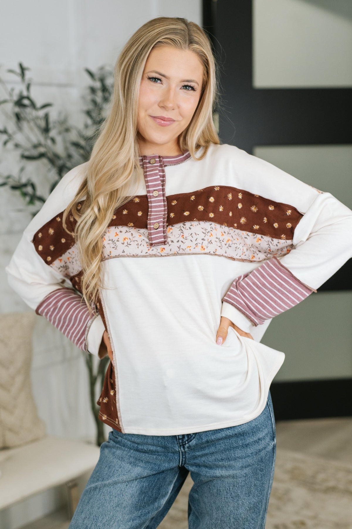 Woman modeling a cream and rust color block top with patterned bands, henley placket, striped cuffs, and blue jeans indoors