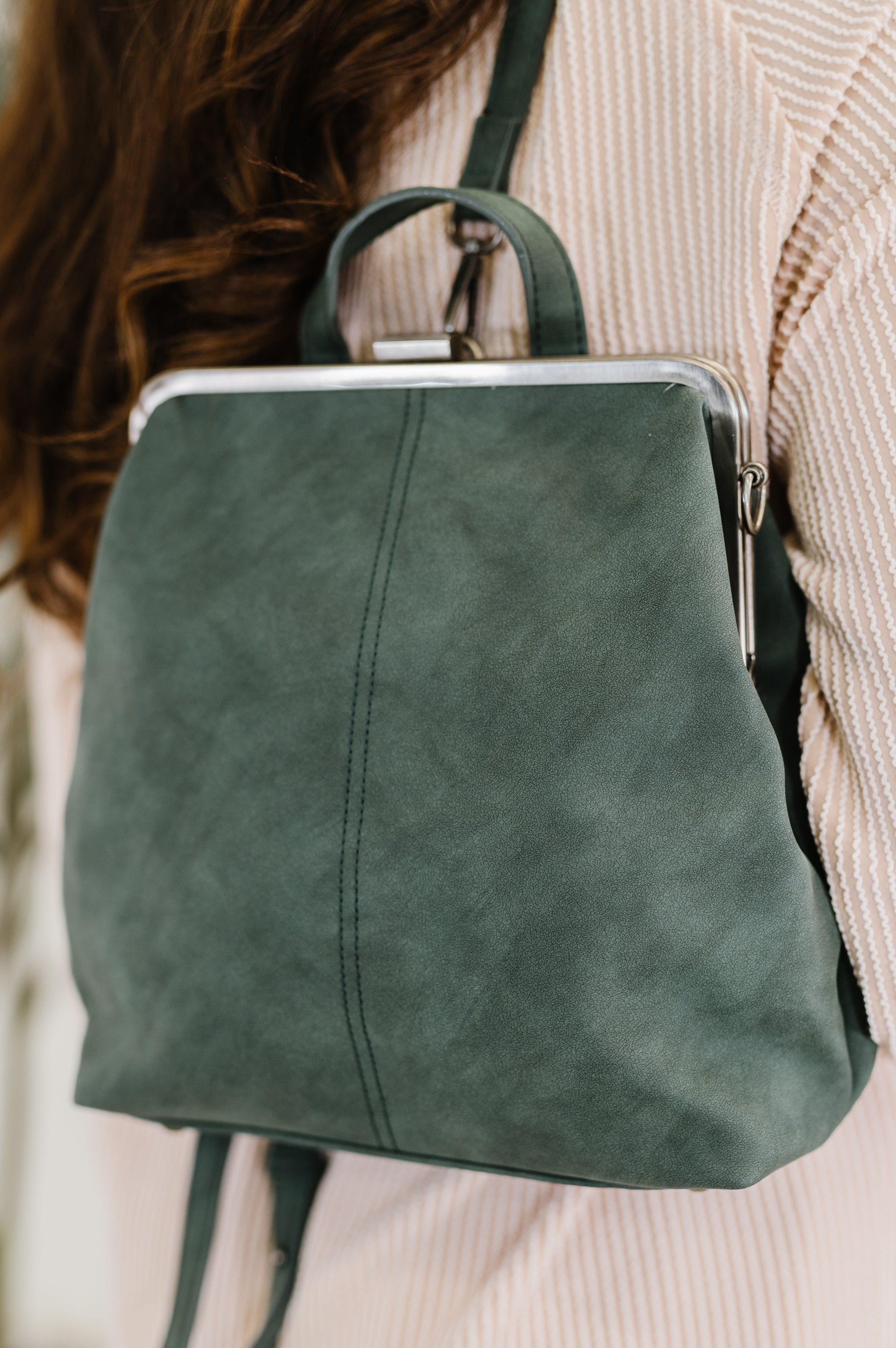 Close-up of green soft leather backpack with metal frame clasp worn on shoulder over textured beige top