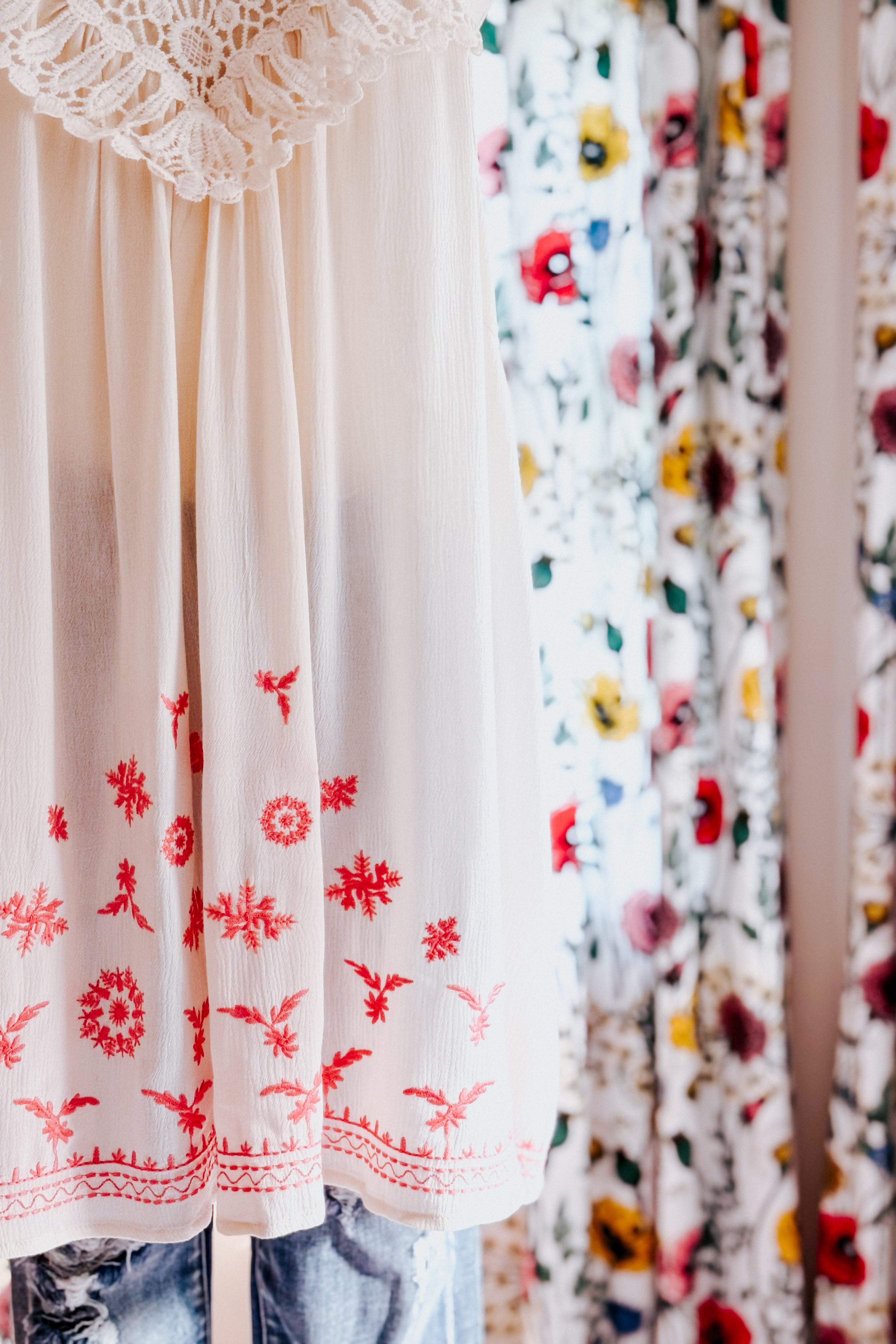 Off-white flowing top with lace yoke and red floral embroidery paired with blue jeans indoors