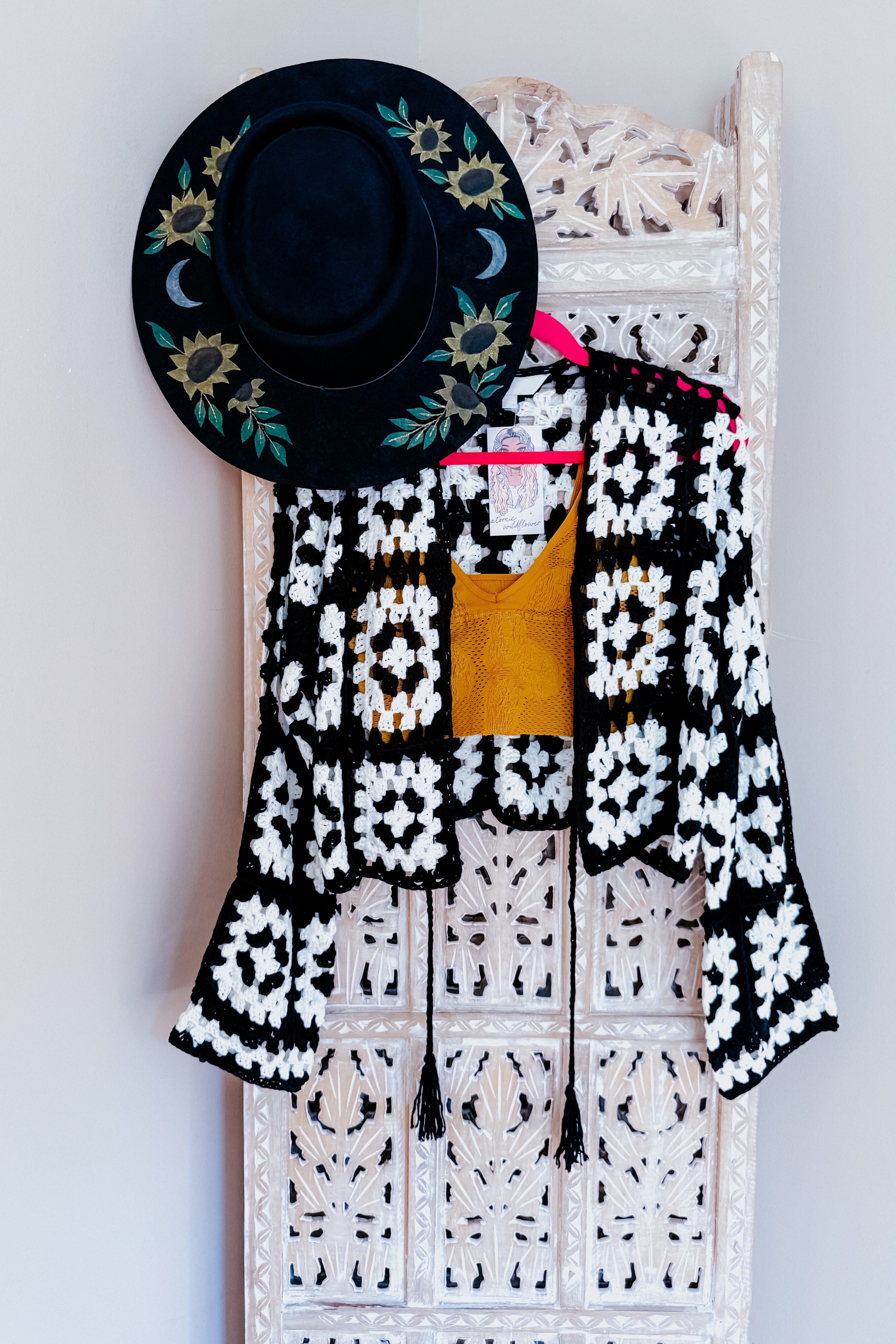 Black and white crochet cropped cardigan with textured open weave paired with mustard yellow top hanging on pink hanger