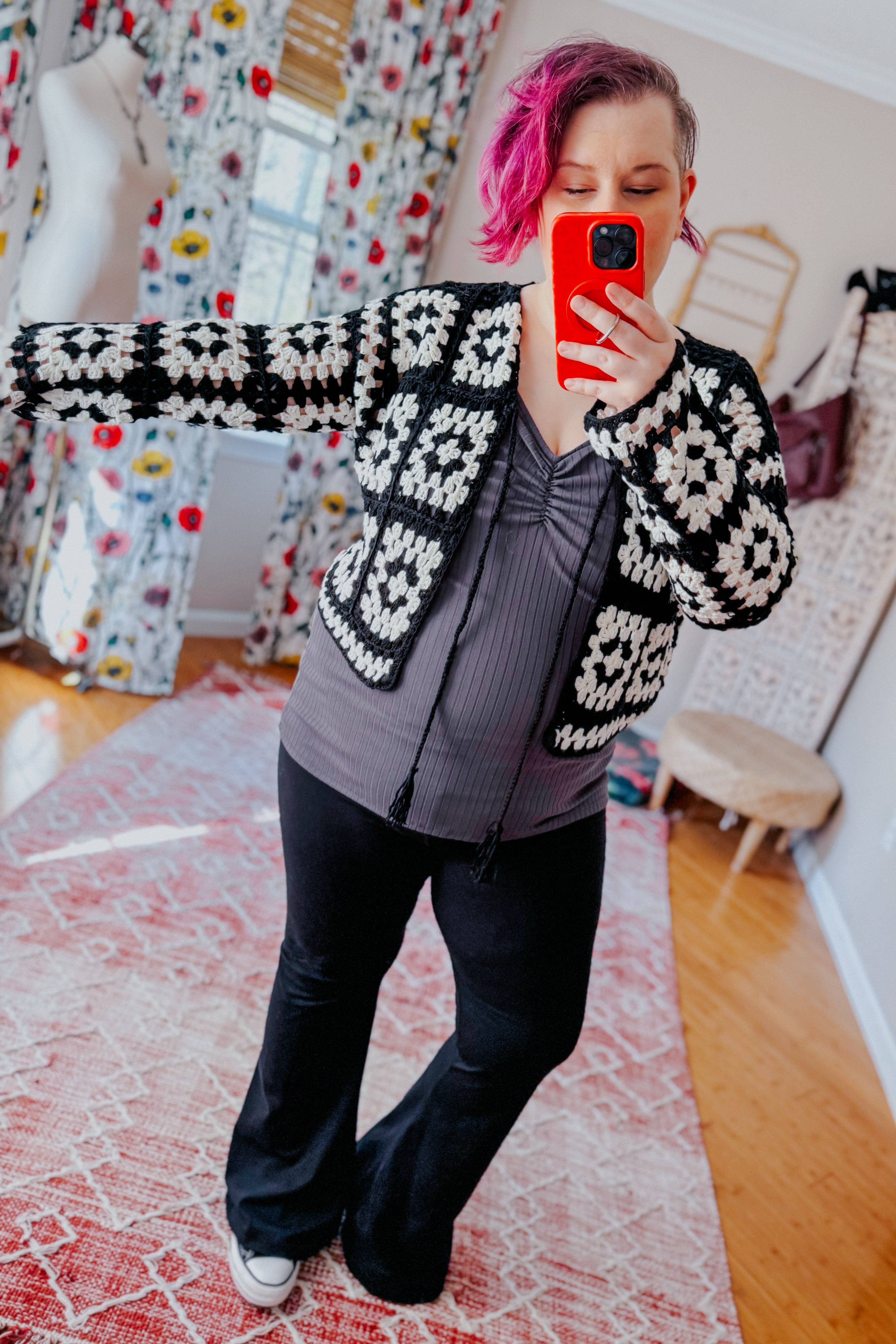 Woman taking mirror selfie wearing black and white crochet cropped cardigan over gray ruched top with black flared pants indoors