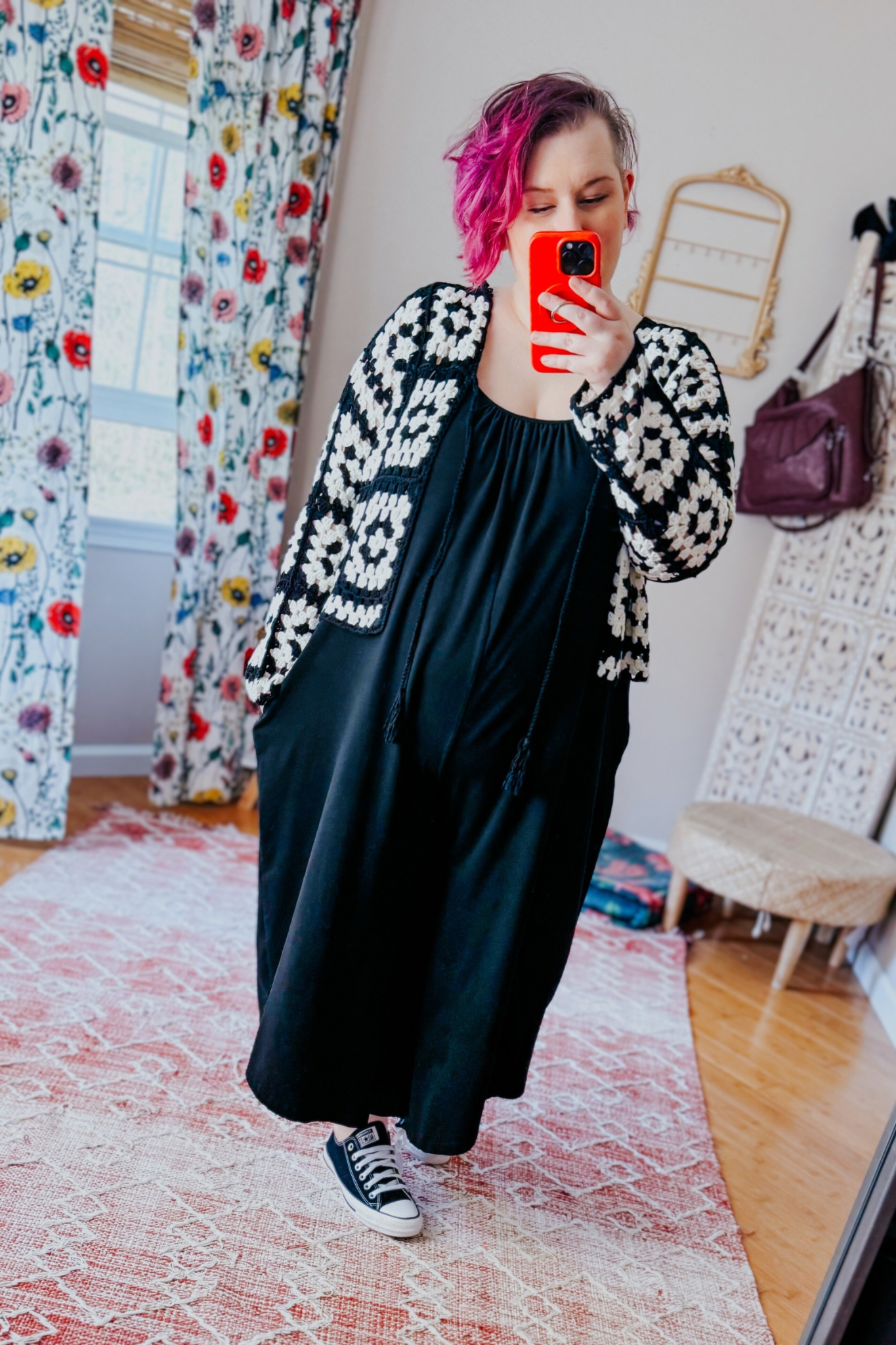 Woman taking indoor mirror selfie wearing black dress and black and white crochet cropped cardigan with sneakers