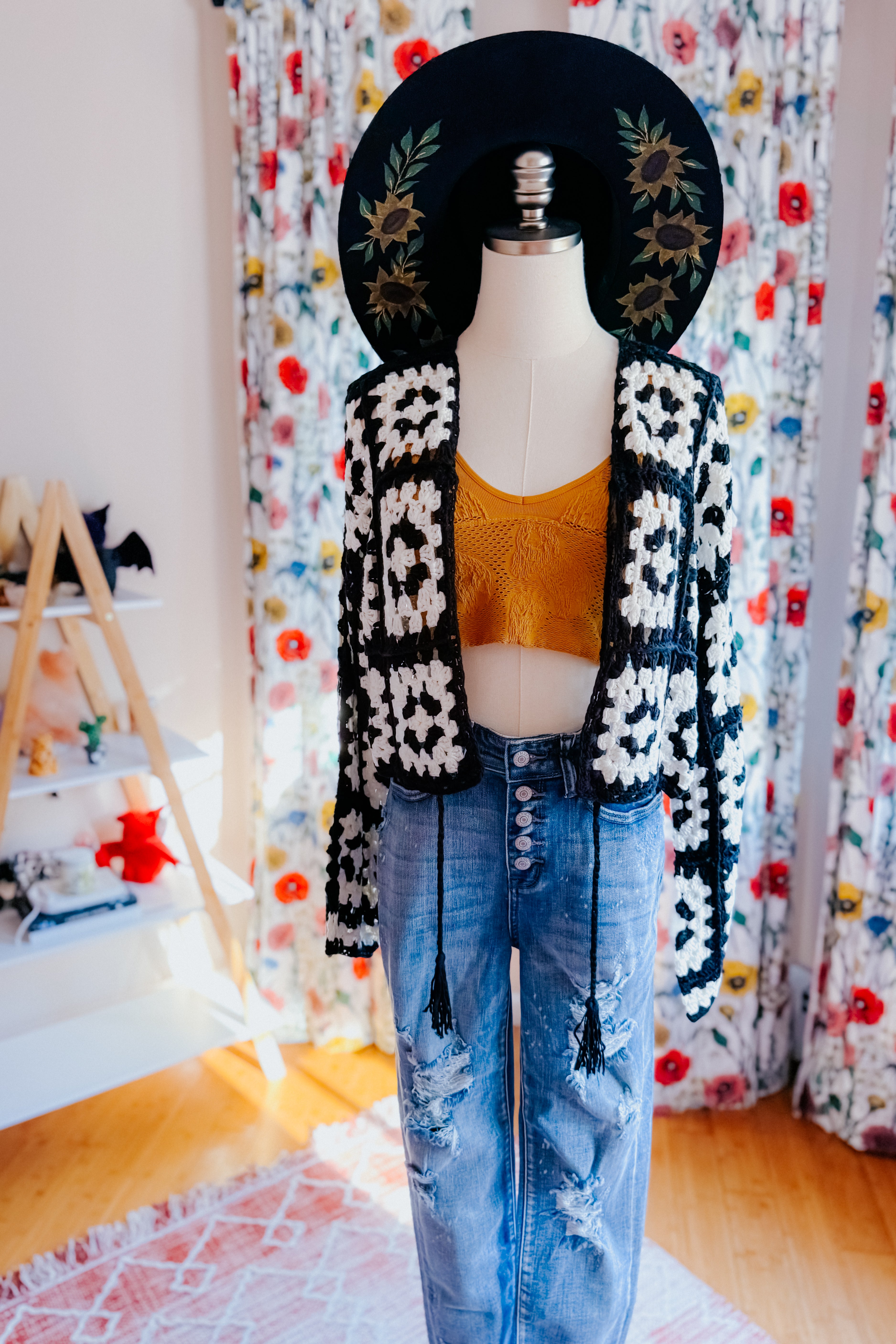 Mannequin wearing black and white crochet cropped cardigan over mustard yellow crop top and distressed blue jeans indoors