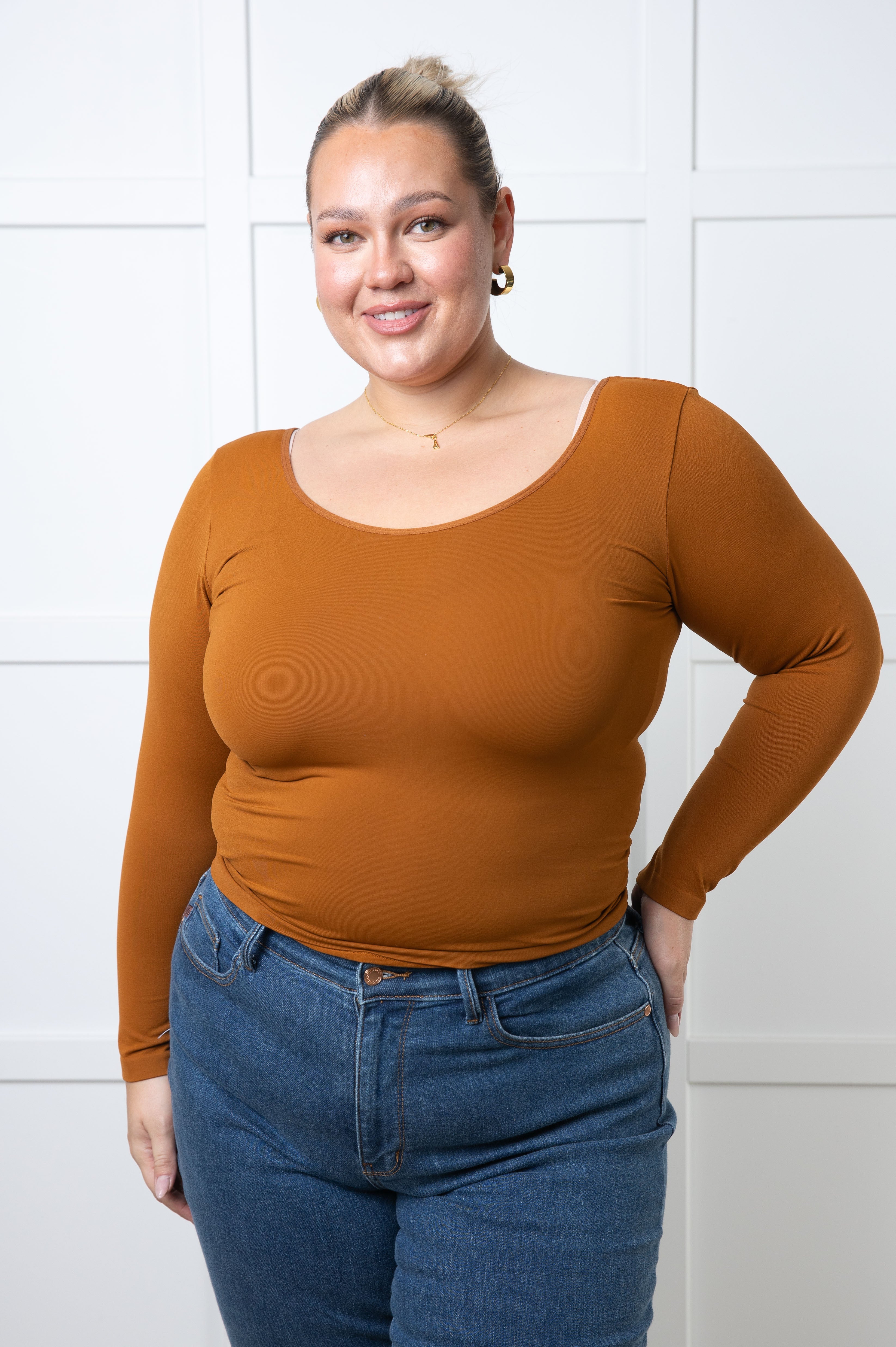 Curvy woman modeling caramel seamless long sleeve reversible V-neck top with blue high-waisted jeans indoors
