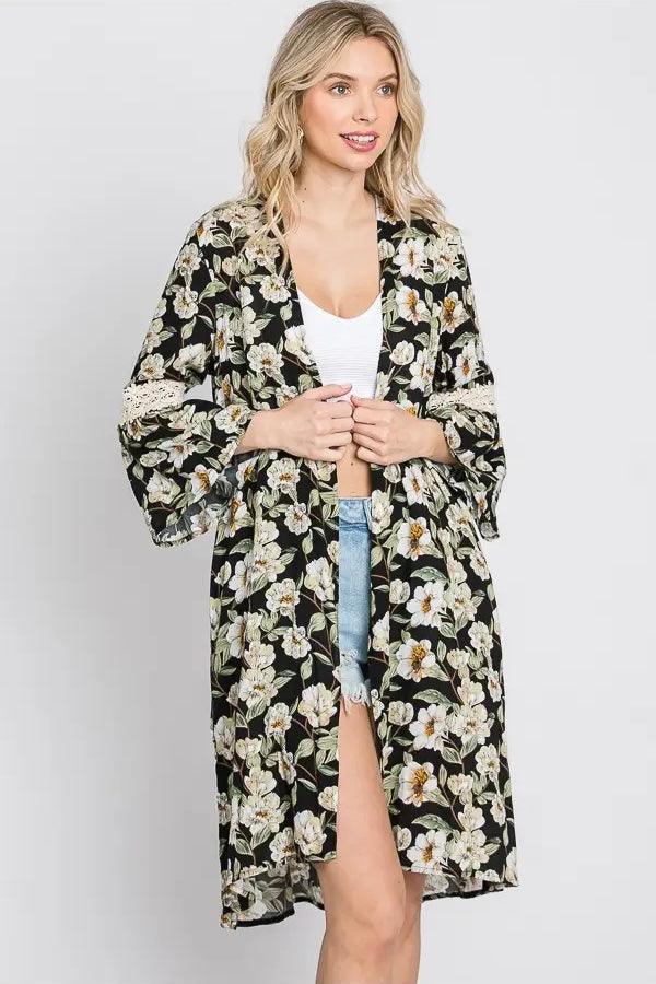 Blonde woman wearing black floral print 3/4 bell sleeve duster with lace trim over white tank top and denim shorts