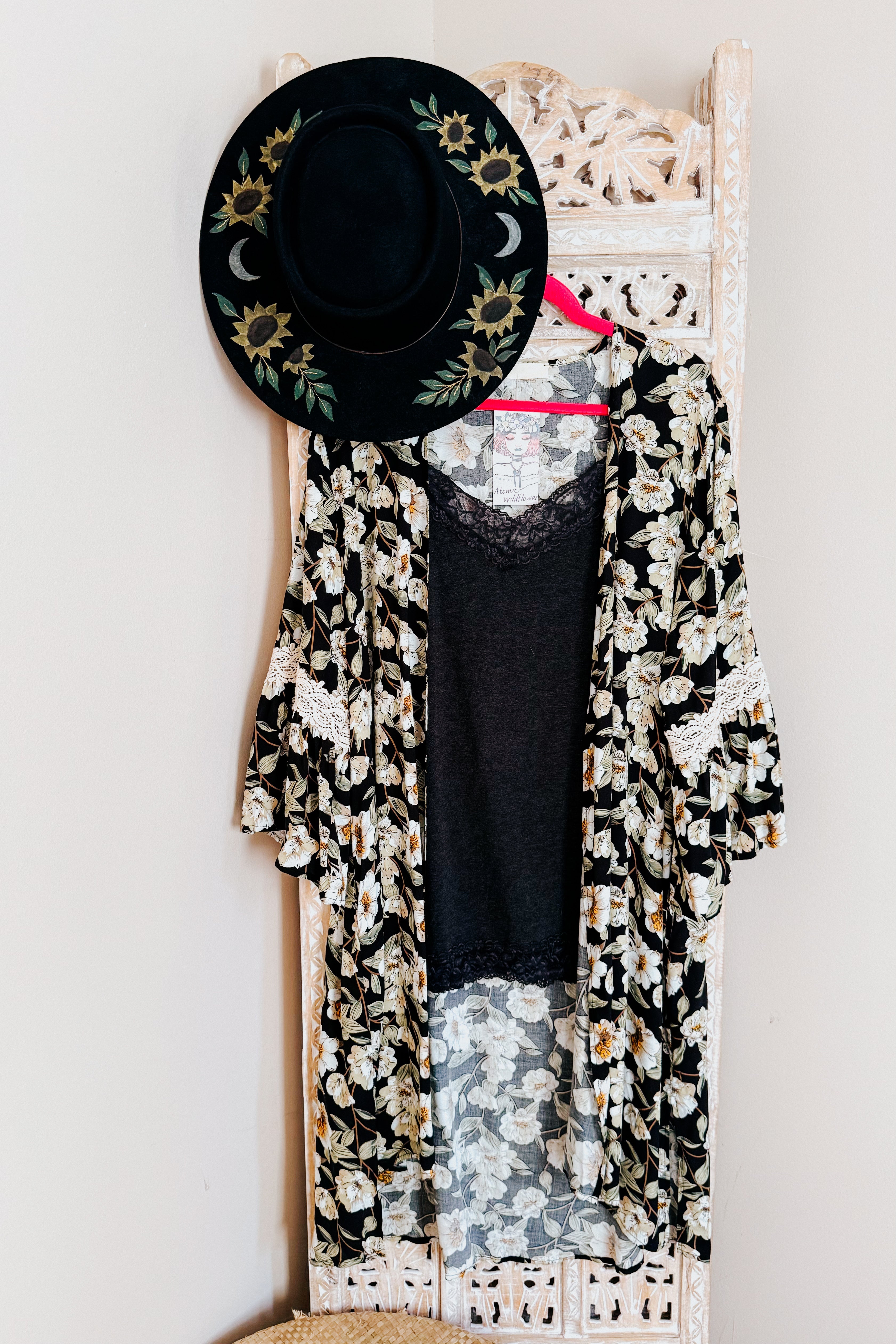 Black floral print 3/4 bell sleeve duster with lace trim layered over black lace-trimmed top on pink hanger with embroidered hat above