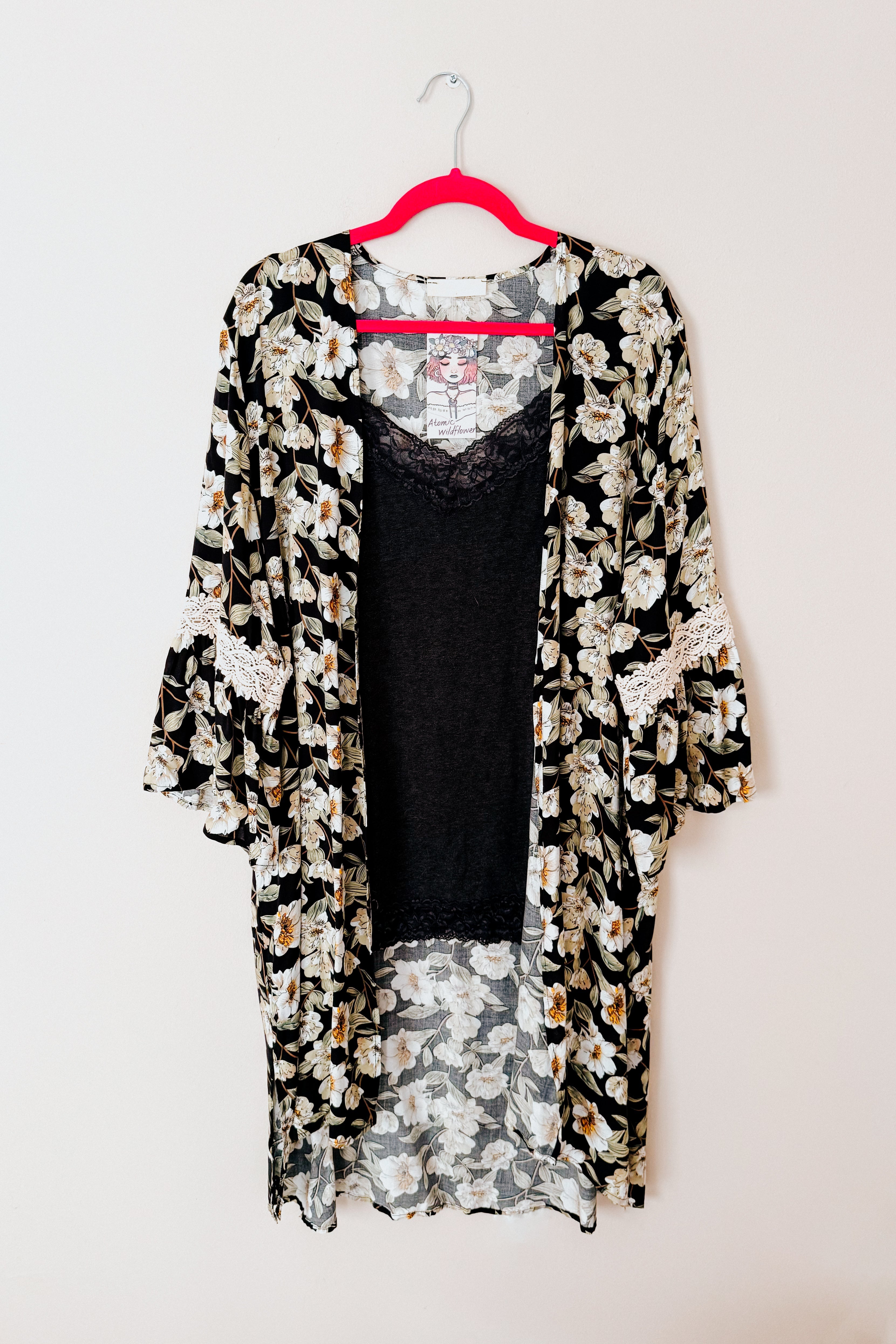 Black floral print 3/4 bell sleeve duster with lace trim displayed on pink hanger against white background