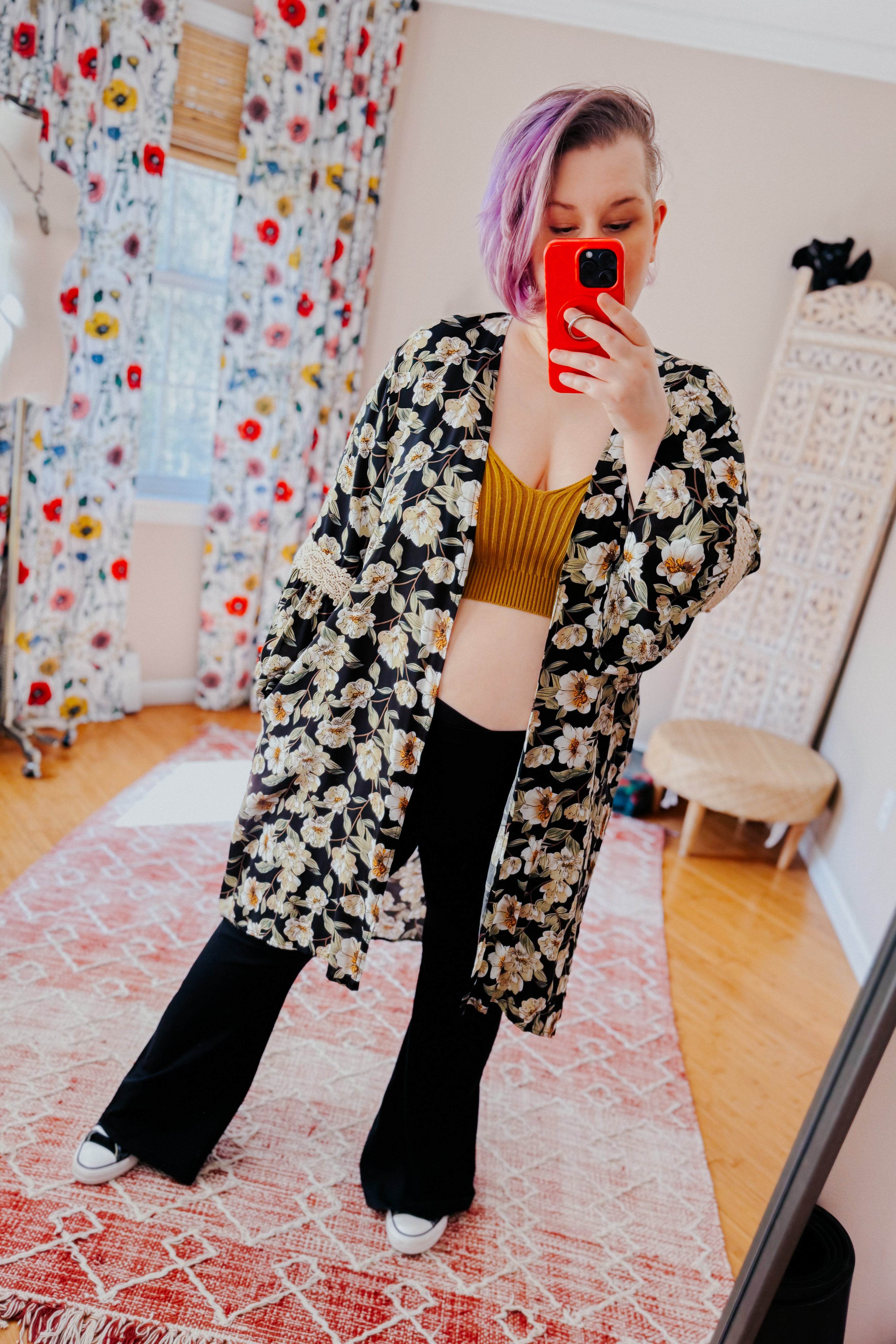 Woman with short purple hair wearing floral print 3/4 bell sleeve duster over mustard ribbed crop top and black pants indoors