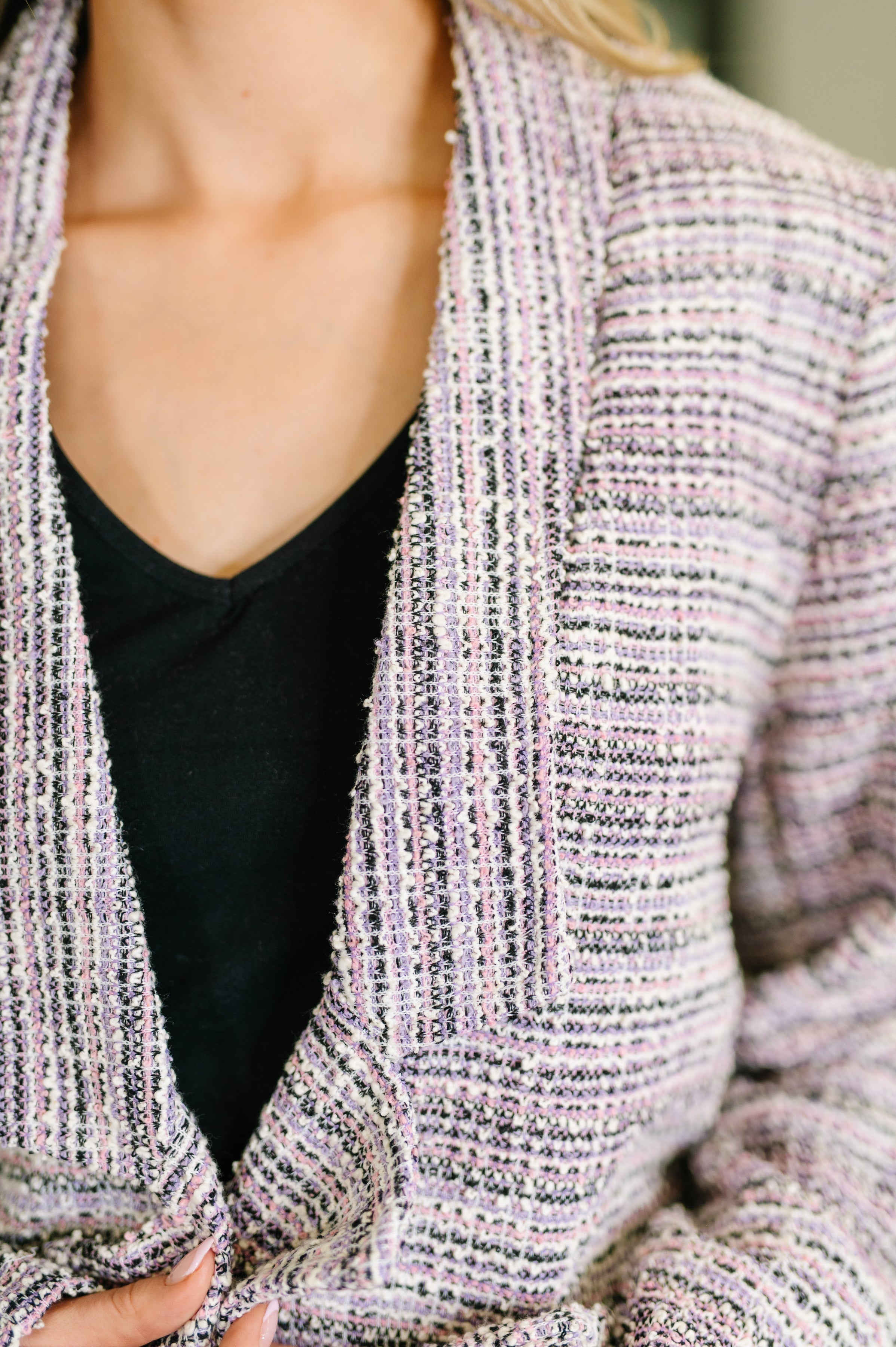Close-up of textured lavender ivory tweed midi blazer worn over a black v-neck top showing collar and chest area
