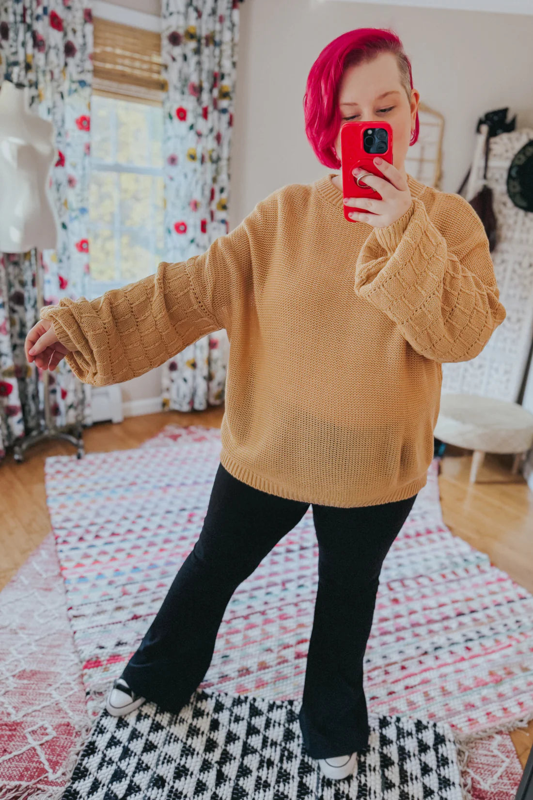 Woman taking mirror selfie wearing wheat-colored bubble sleeve sweater with textured knit and black flared pants indoors