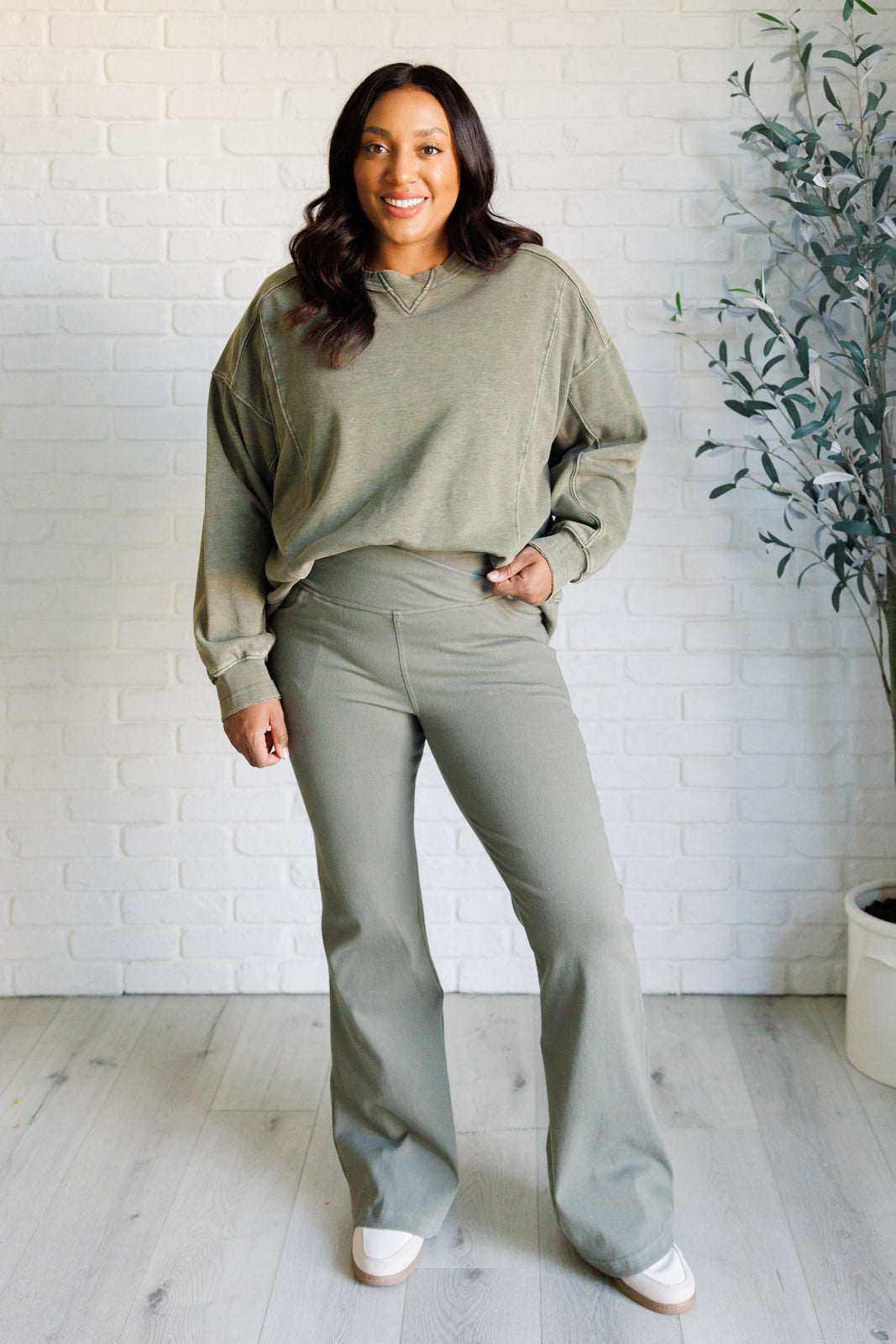 Front view of smiling woman wearing dusty olive crossover waist twill pants and matching oversized sweatshirt indoors