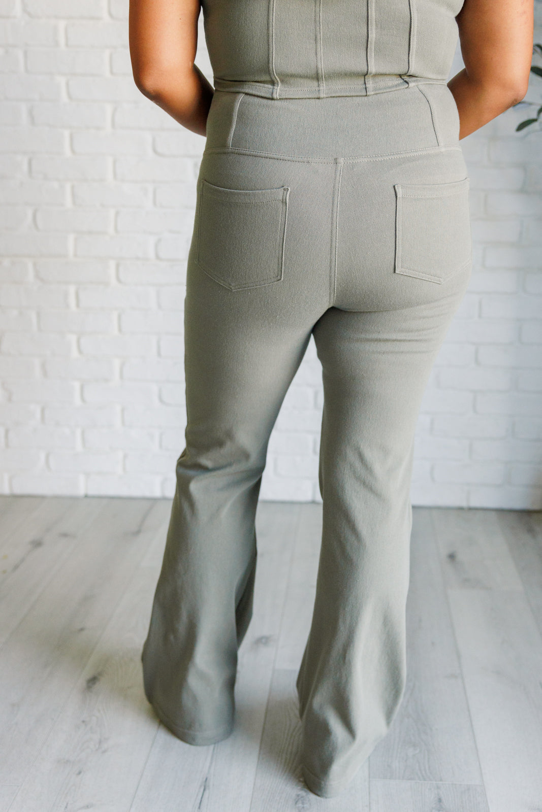 Rear view of person wearing dusty olive twill flared crossover waist pants standing on light wood floor indoors