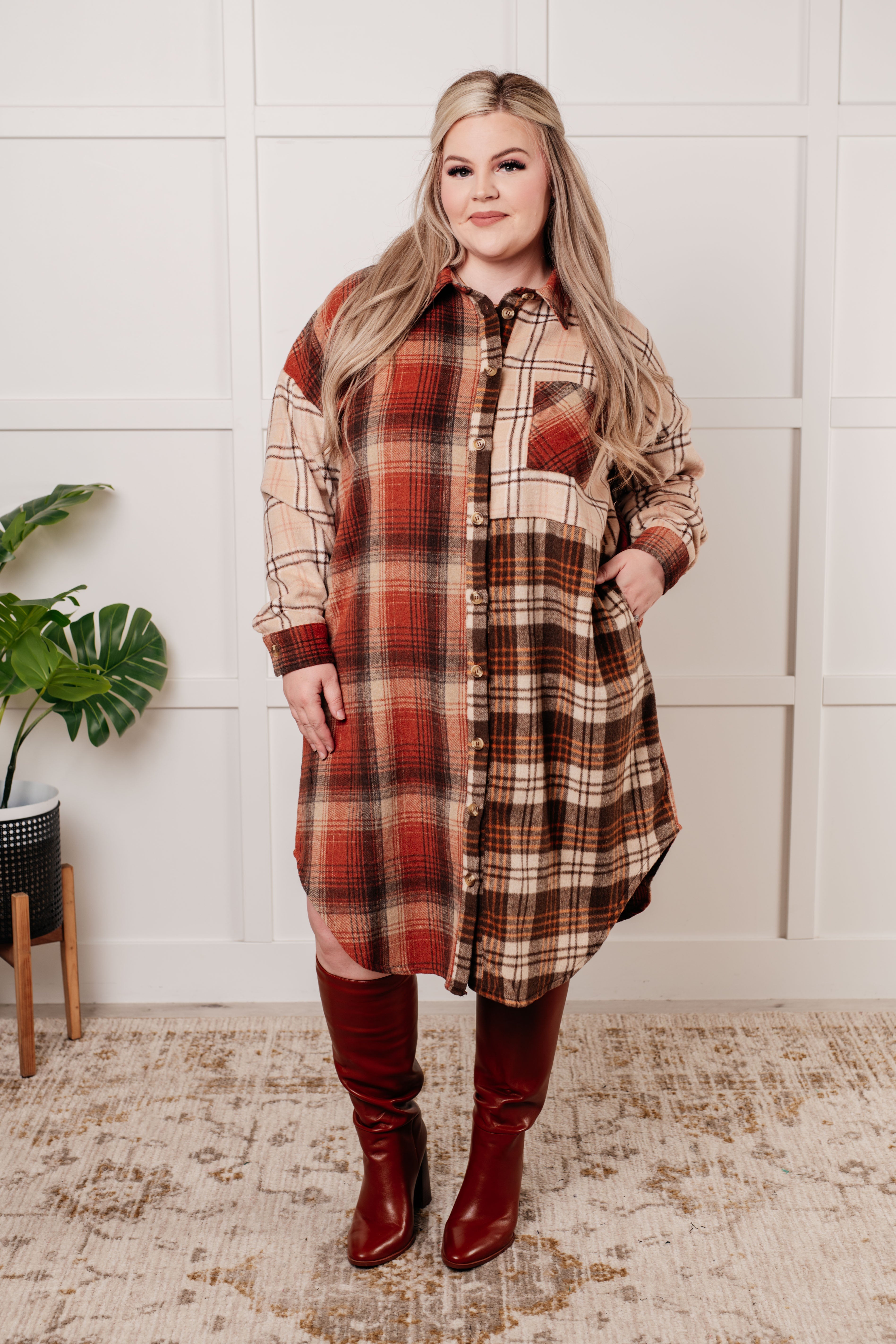 Plus-size woman wearing multi-color plaid oversized shacket with red knee-high boots standing indoors
