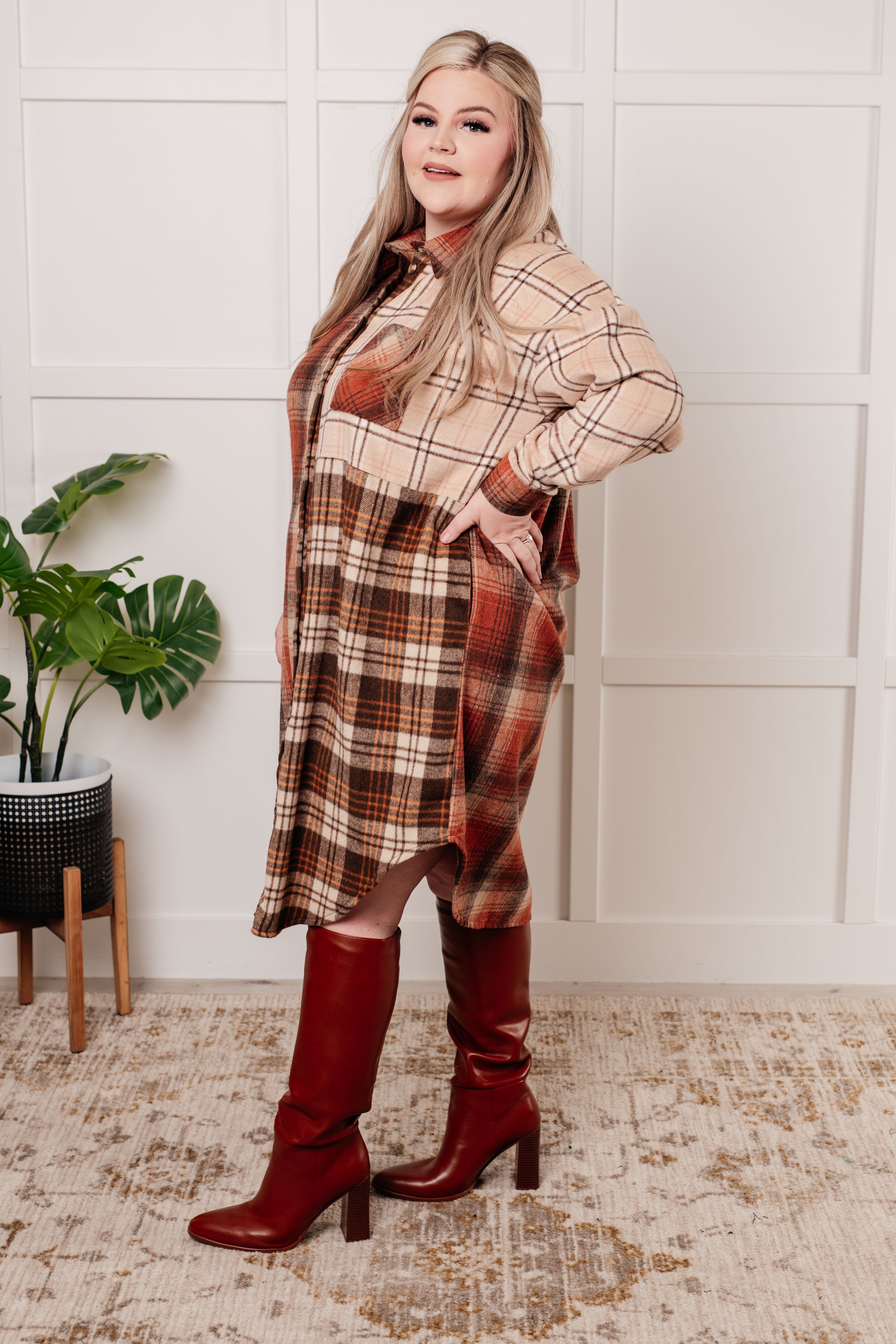 Plus-size woman wearing multi-toned plaid oversized flannel shacket and red knee-high heeled boots indoors