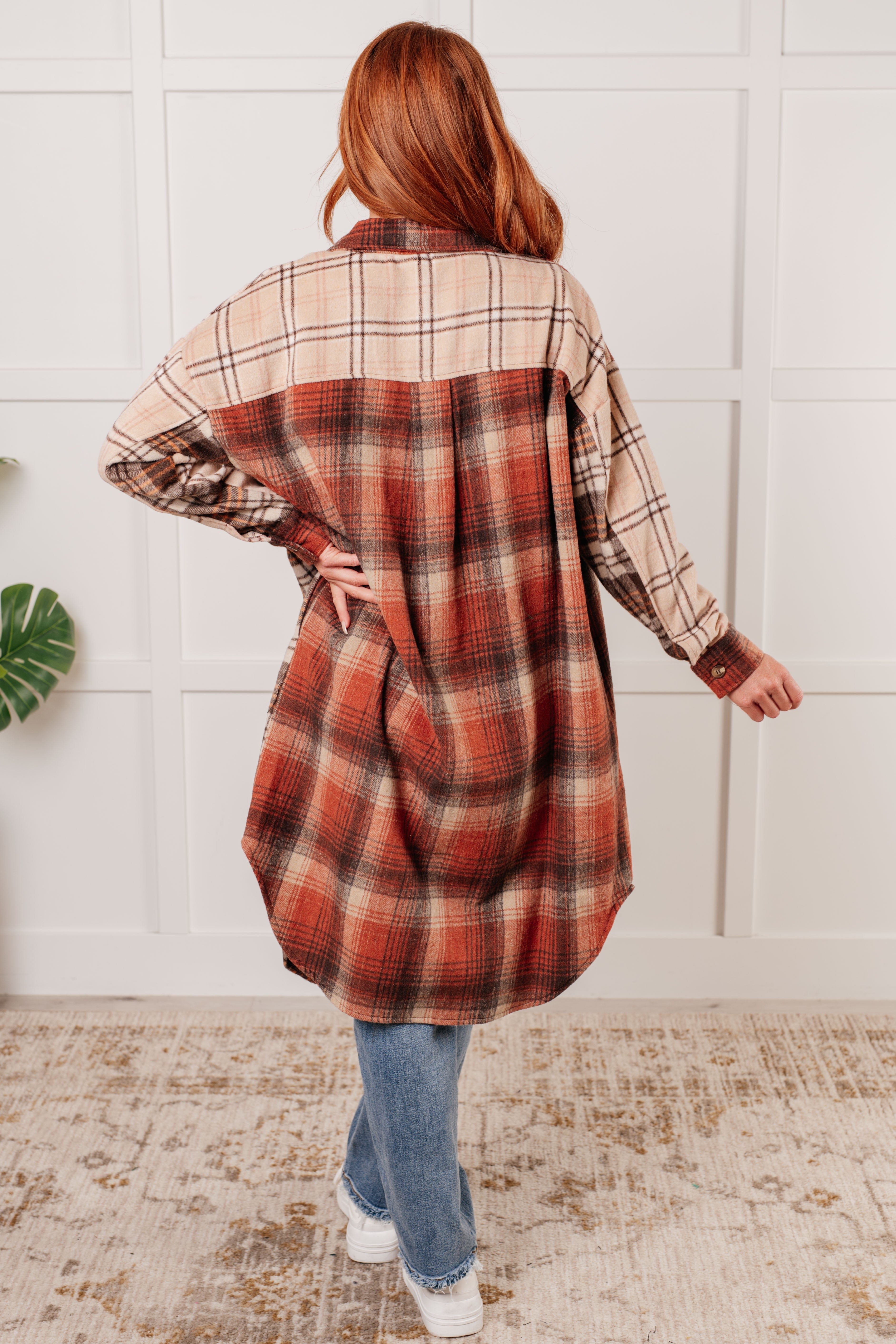 Back view of woman wearing oversized plaid flannel shacket in warm tones with high-low hem indoors