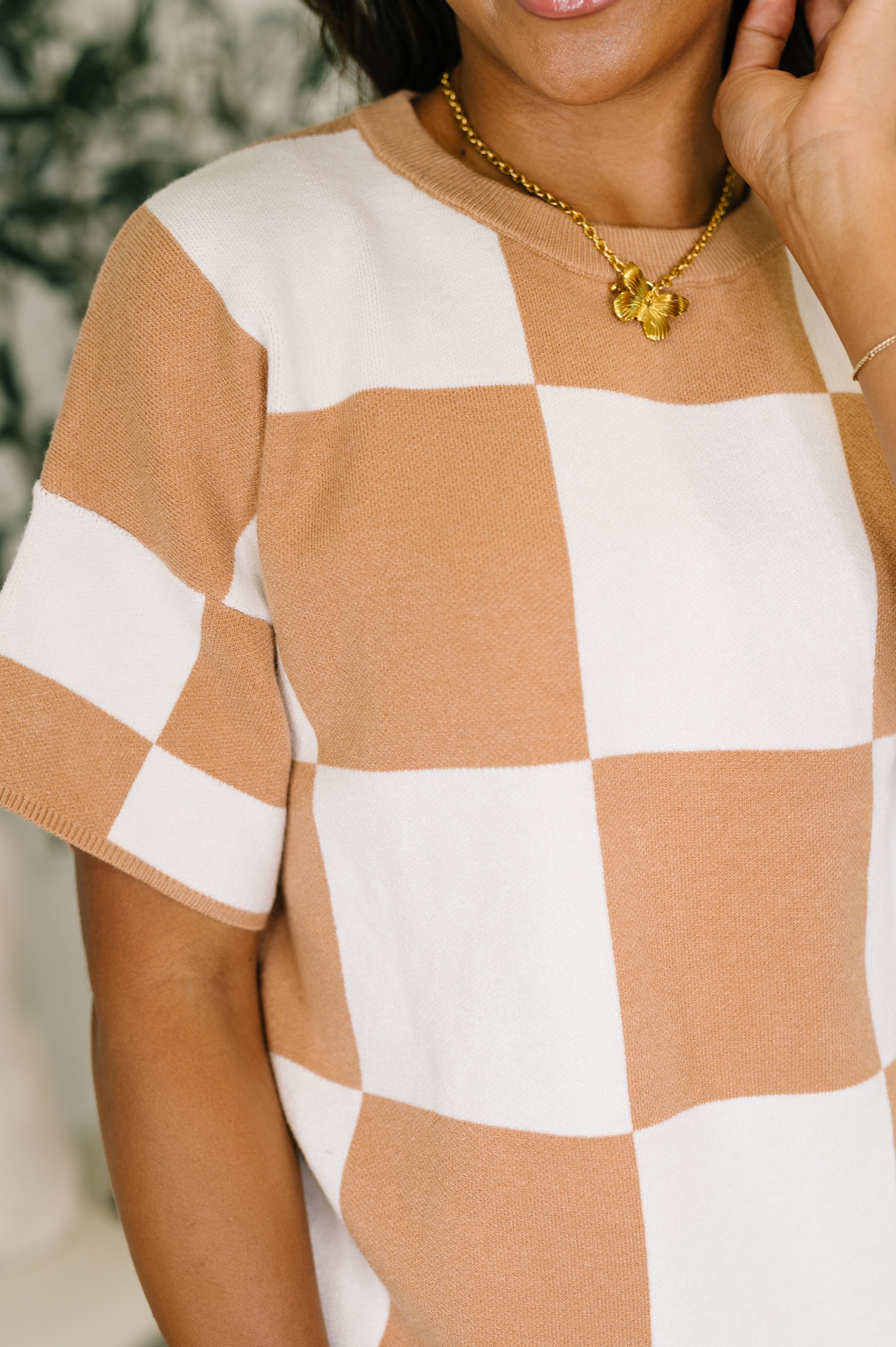 Close-up of woman wearing tan and white large checkered relaxed fit short sleeve sweater indoors