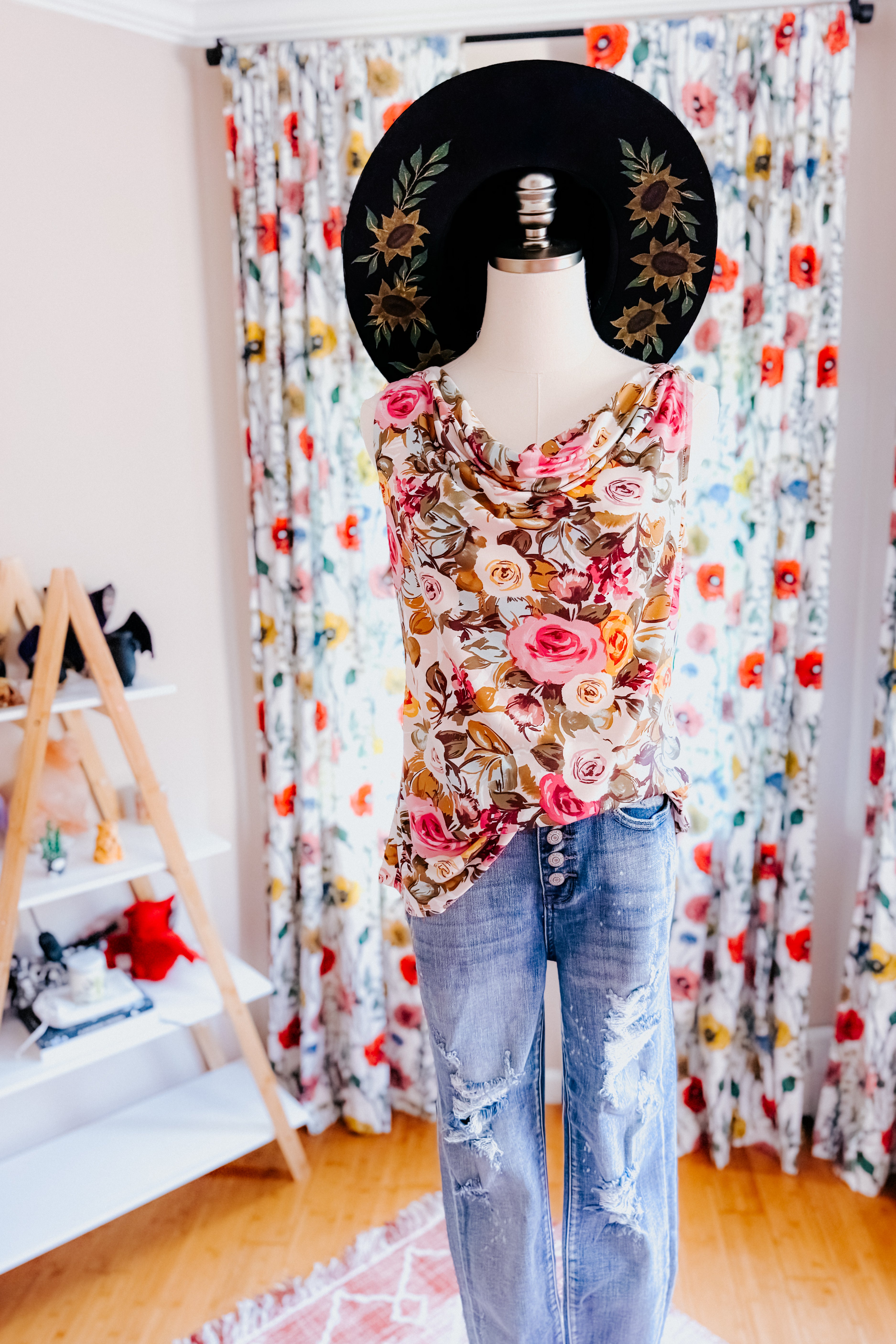 Mannequin wearing floral cowl neck top paired with distressed light blue denim jeans and black wide-brimmed hat indoors