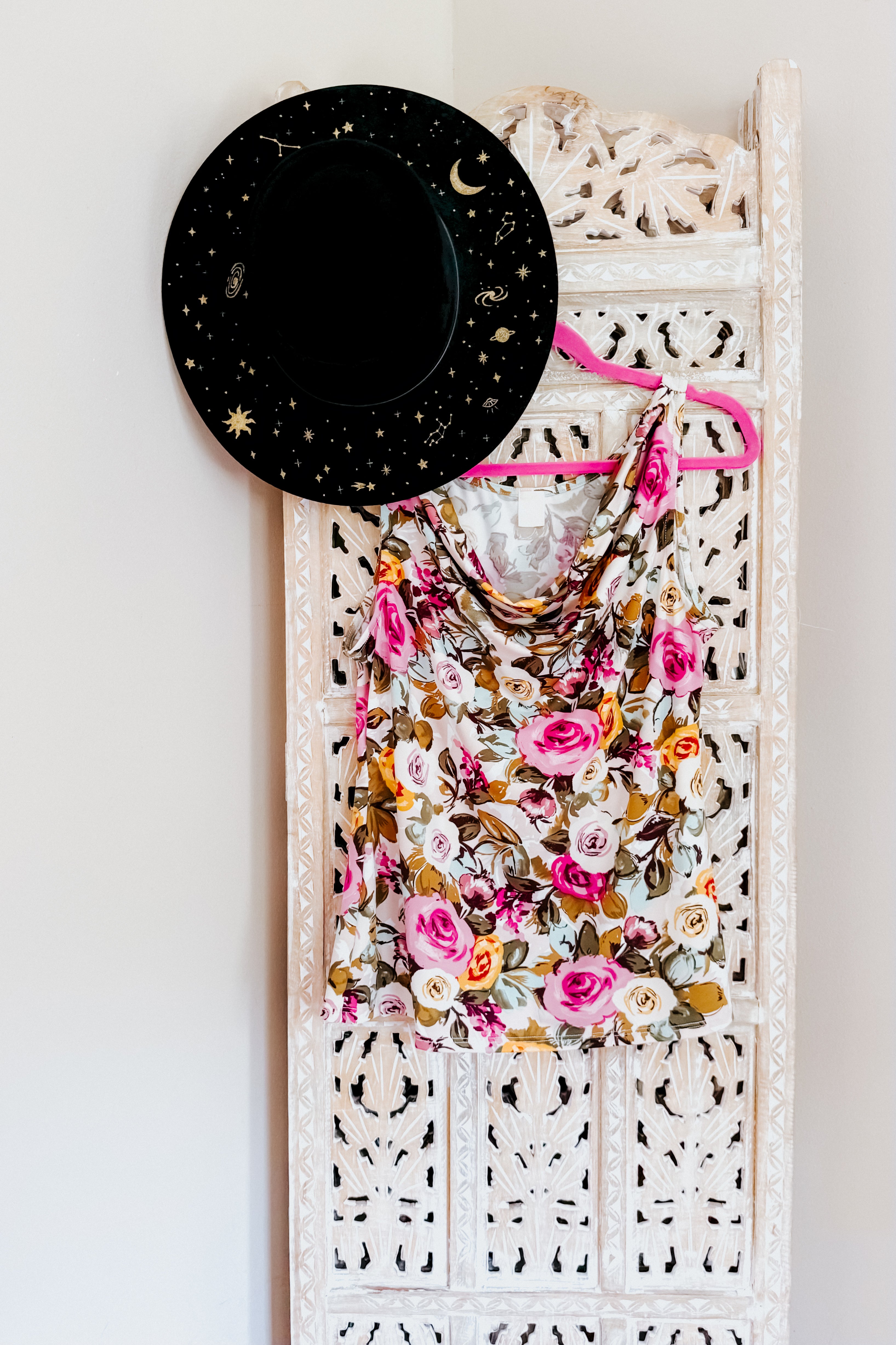 Floral cowl neck tank top with pink and cream roses hanging on pink hanger against carved white wooden screen