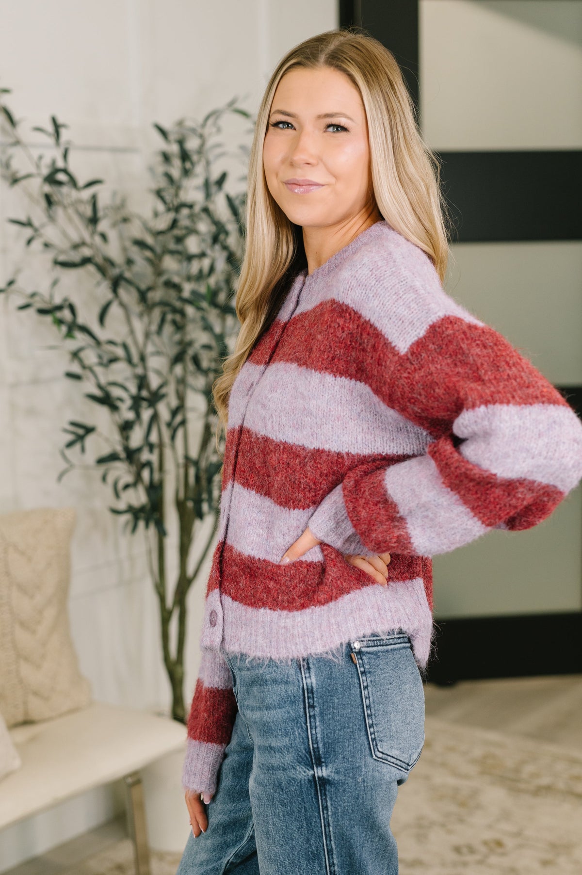 Woman wearing a red and purple striped button down sweater with a ribbed neckline and blue jeans in a stylish home