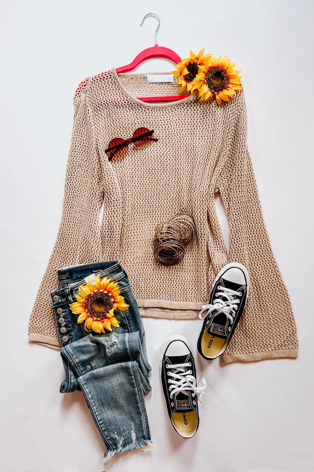 Beige loose knit long sleeve top paired with distressed denim jeans and black sneakers styled with sunflowers and bangles