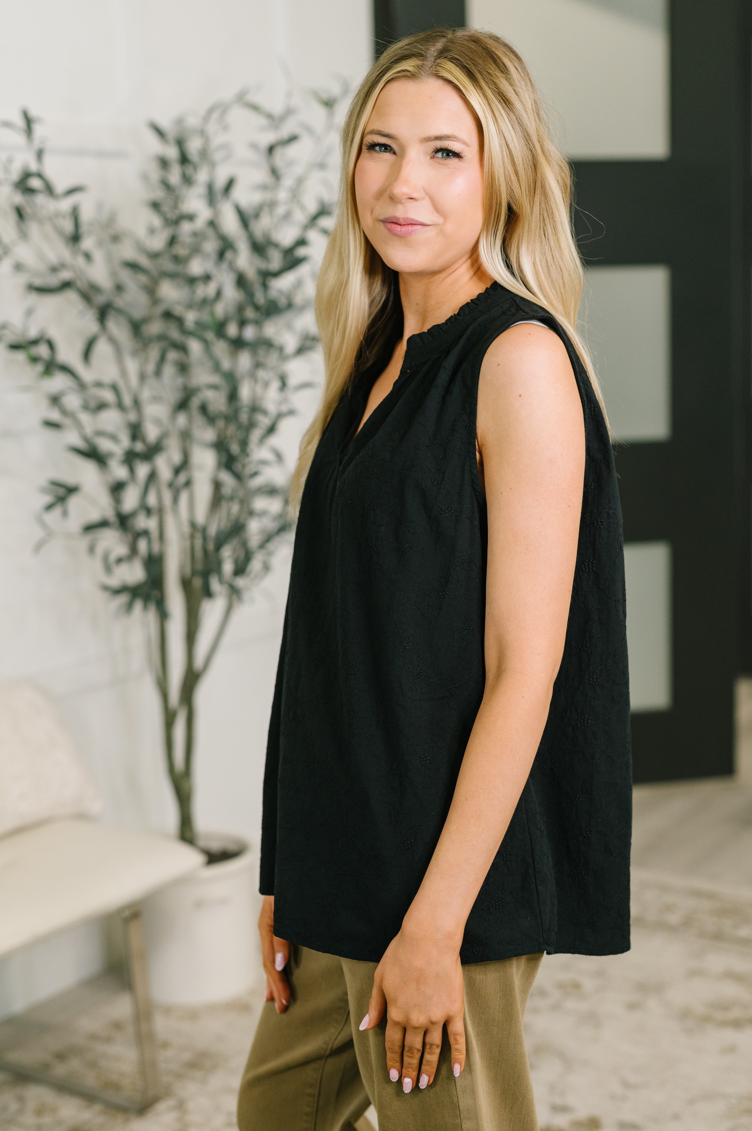 Side view of woman wearing sleeveless black embroidered tank with split neckline and relaxed fit indoors