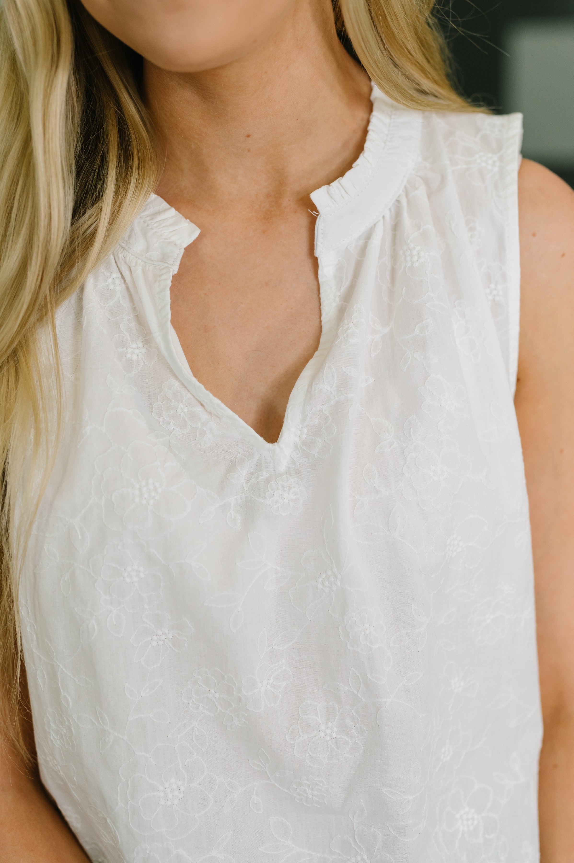 Close-up of sleeveless off-white tank with delicate floral embroidery and a subtle split neckline on lightweight woven fabric