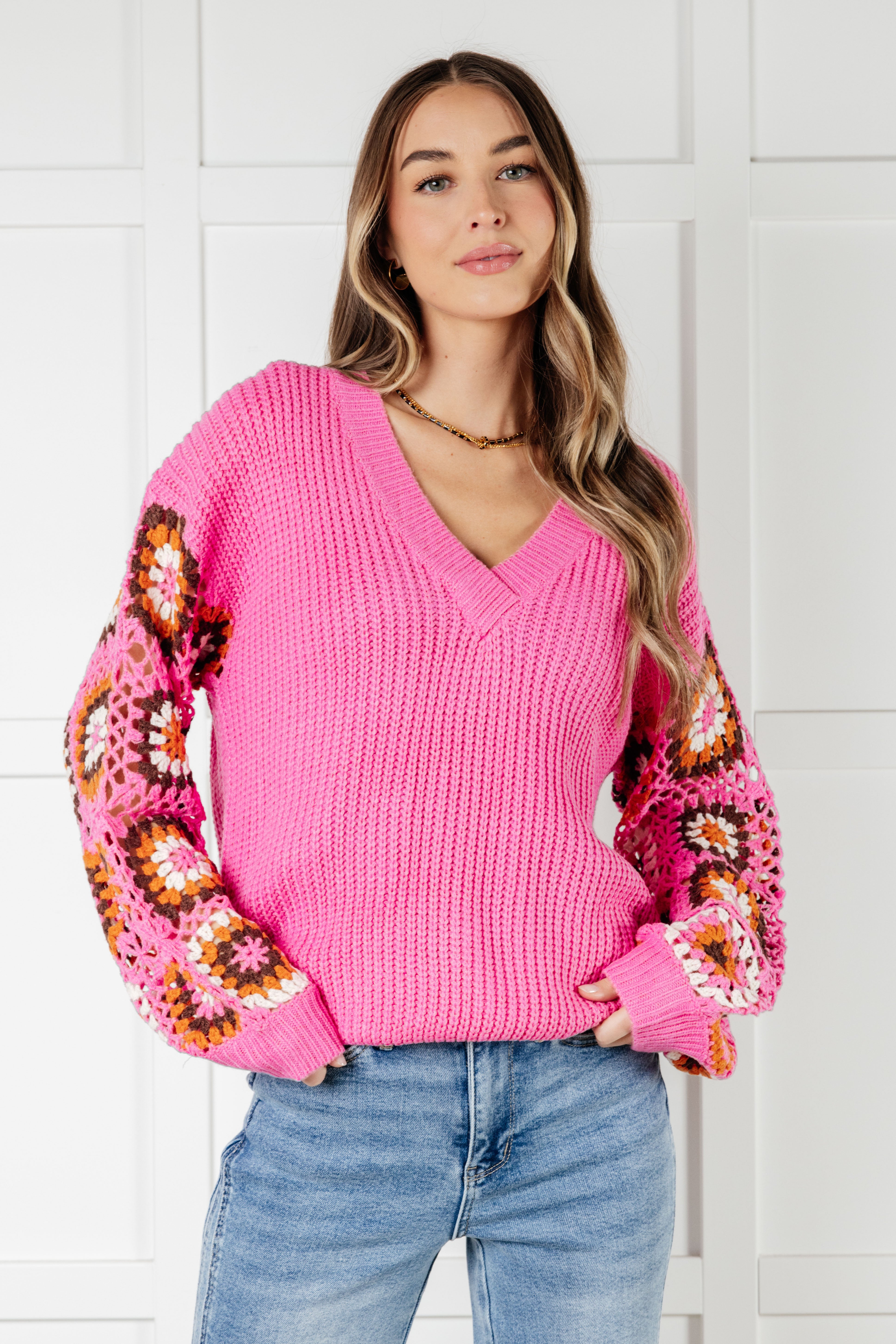 Woman wearing bright pink V-neck knit sweater with colorful crochet floral balloon sleeves and light blue jeans