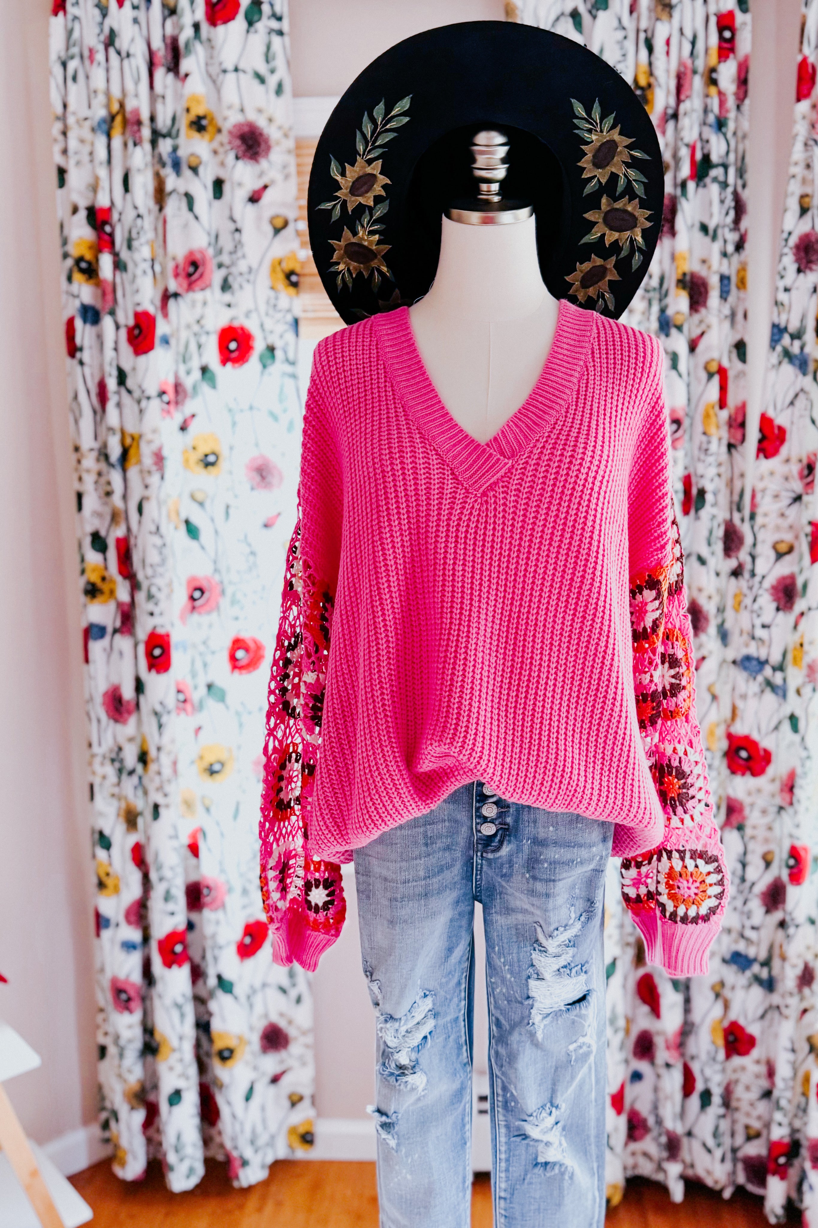 Bright pink V-neck chunky knit sweater with multicolored crochet balloon sleeves on mannequin with floral curtains background