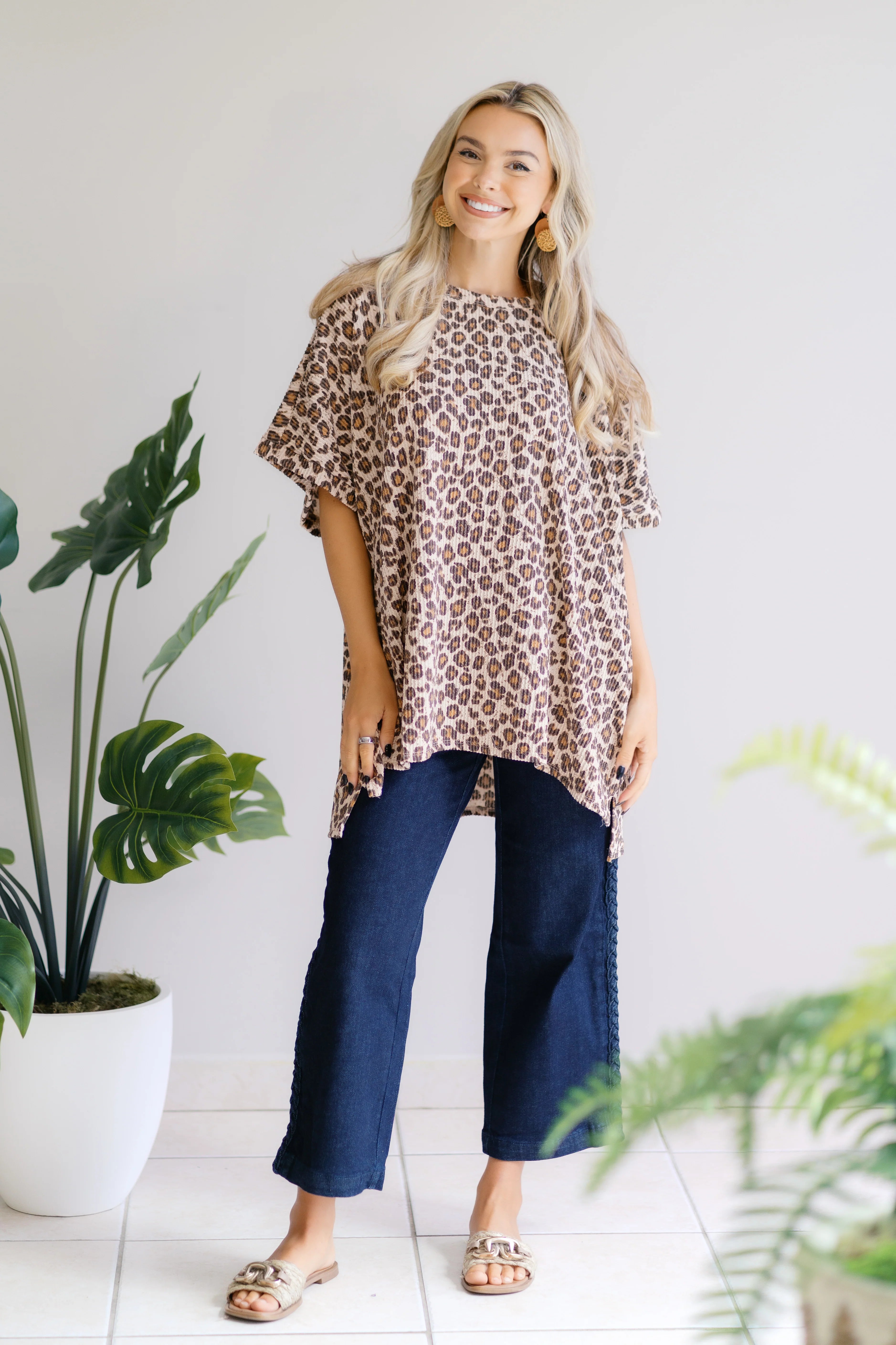 Smiling blonde woman standing indoors wearing oversized leopard print Canyon Wild Top with dark wide-leg jeans and sandals
