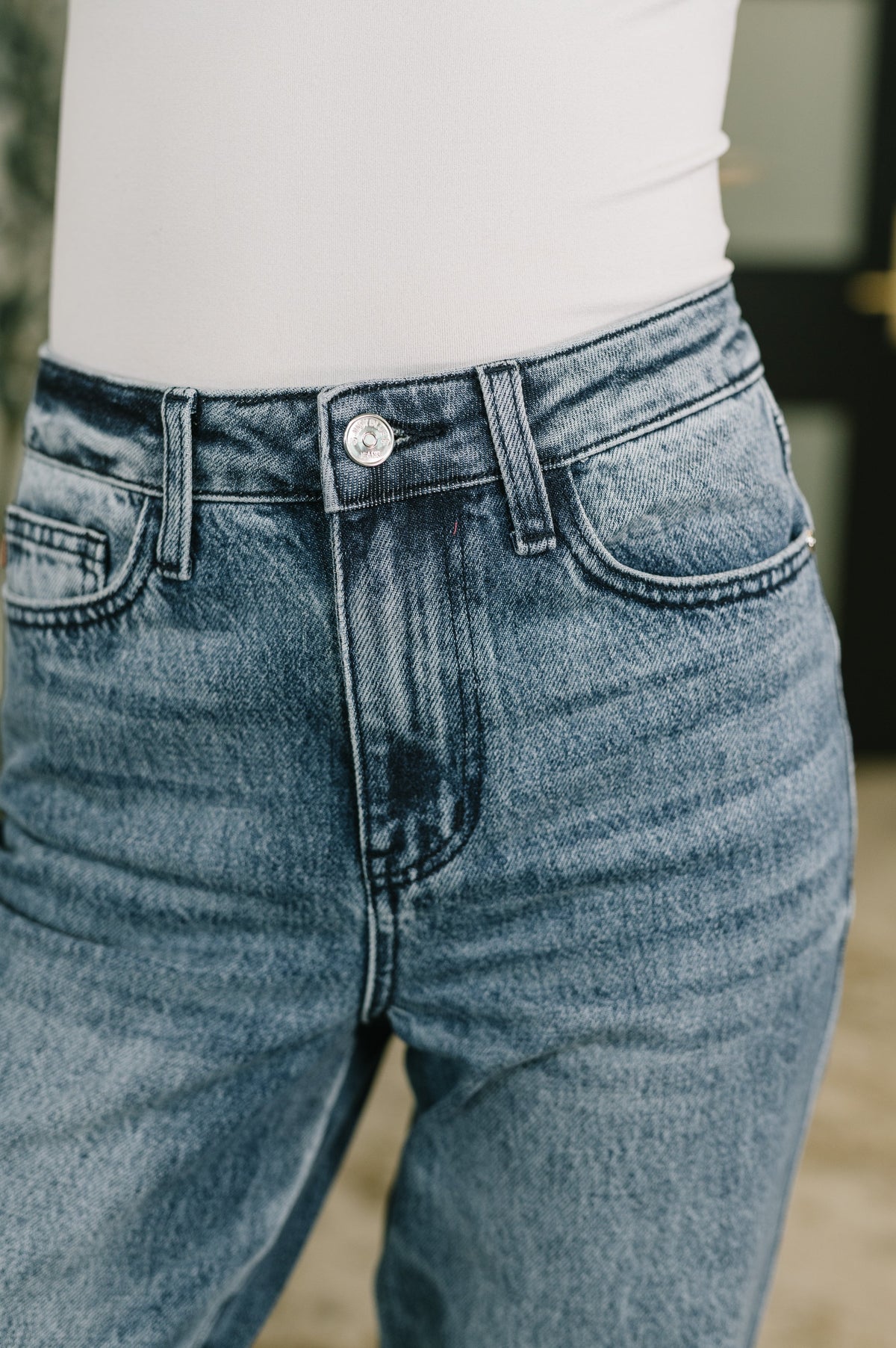 Close view of a woman wearing blue high waist straight leg jeans with a button fly front pockets and classic denim stitching