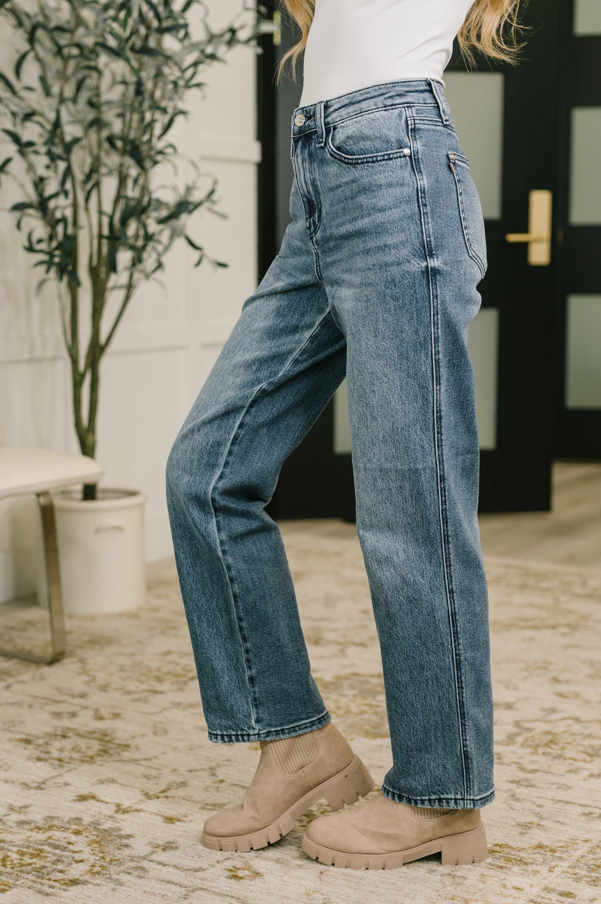 Woman modeling blue high waist straight leg jeans with a white top and beige ankle boots in a bright entryway