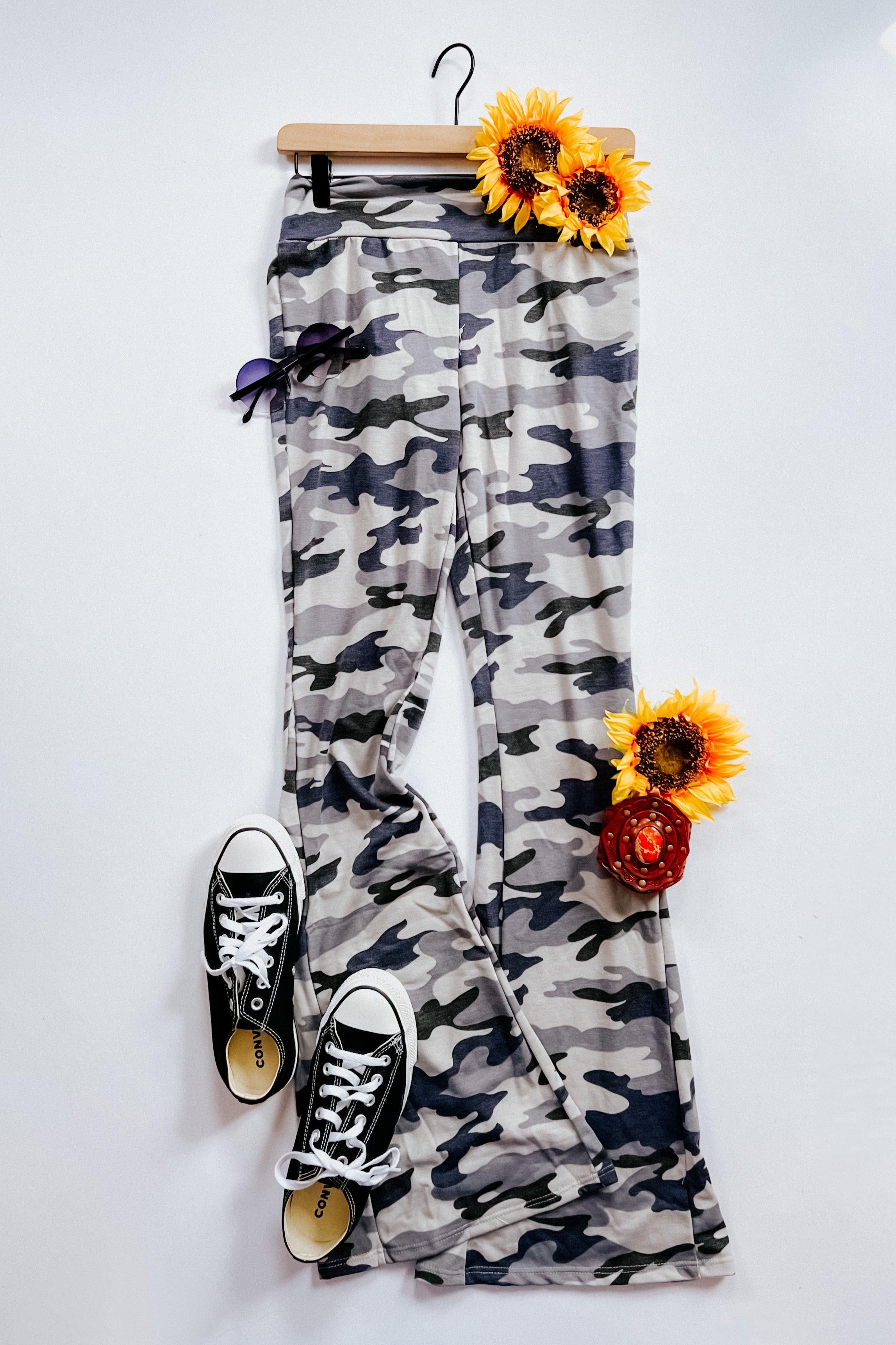 Gray and navy blue camouflage flare pants styled with black canvas sneakers, sunglasses, and sunflowers on white background