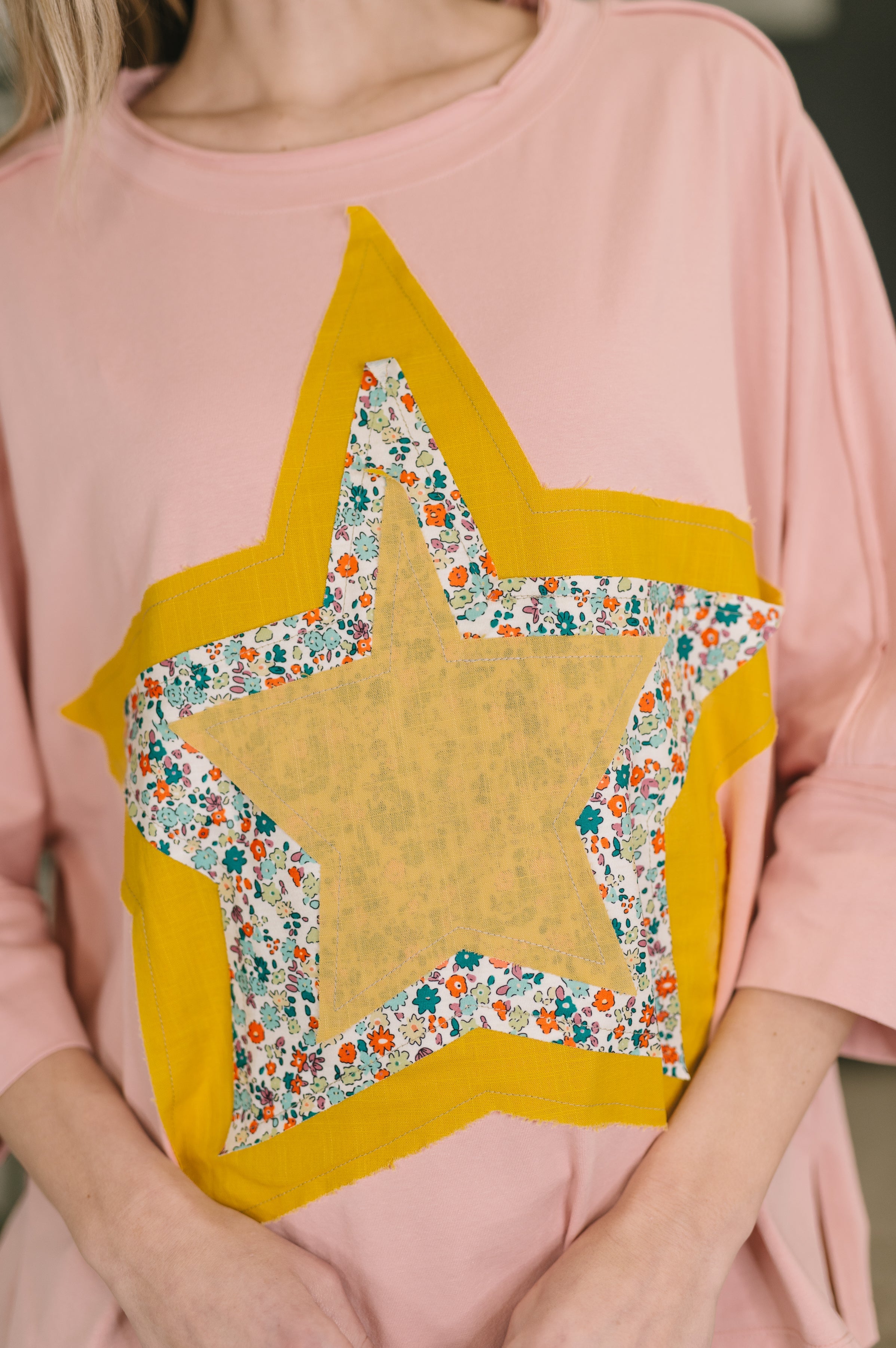 Close-up of pastel pink top featuring layered star patches in yellow and floral prints on front