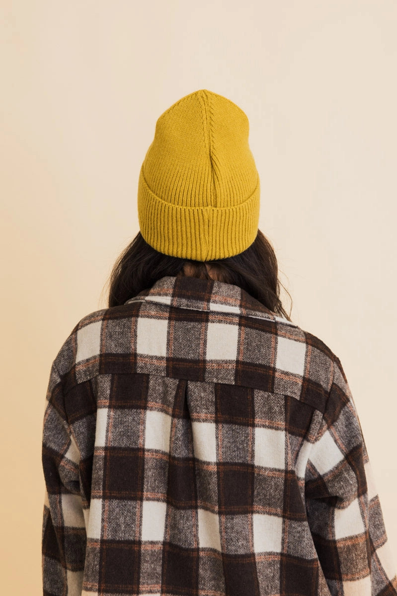 Back view of person wearing mustard ribbed knit beanie and brown plaid flannel shirt against beige background