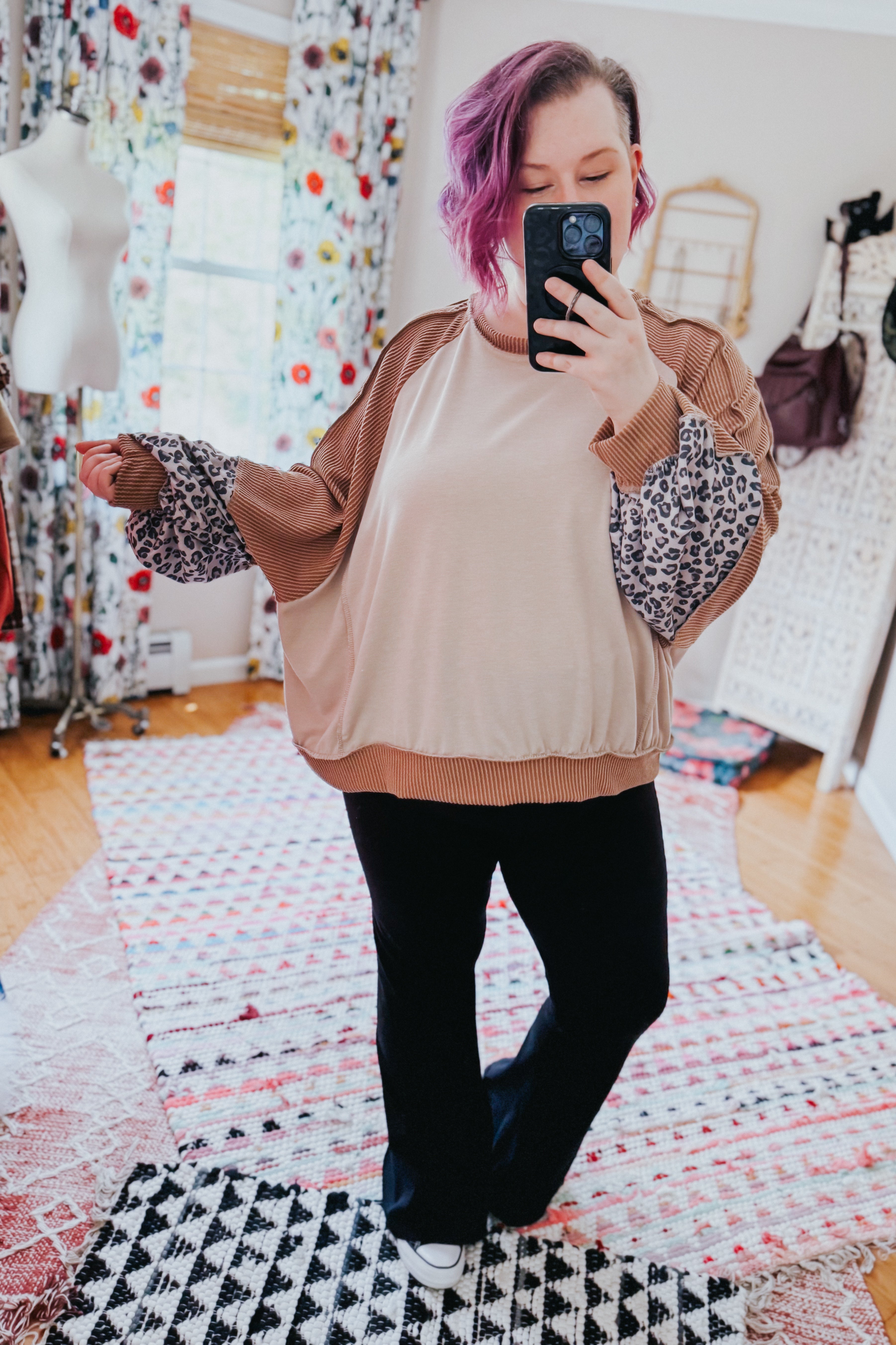 Woman taking mirror selfie wearing beige dolman colorblock terry top with rust ribbed and leopard print sleeves paired with black pants